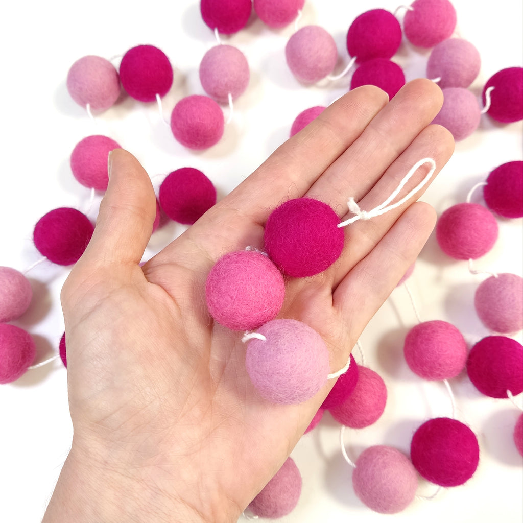 Zoom sur les pompons en feutre de 2,5 cm aux tons roses de la guirlande fleurs de cerisier dans une main