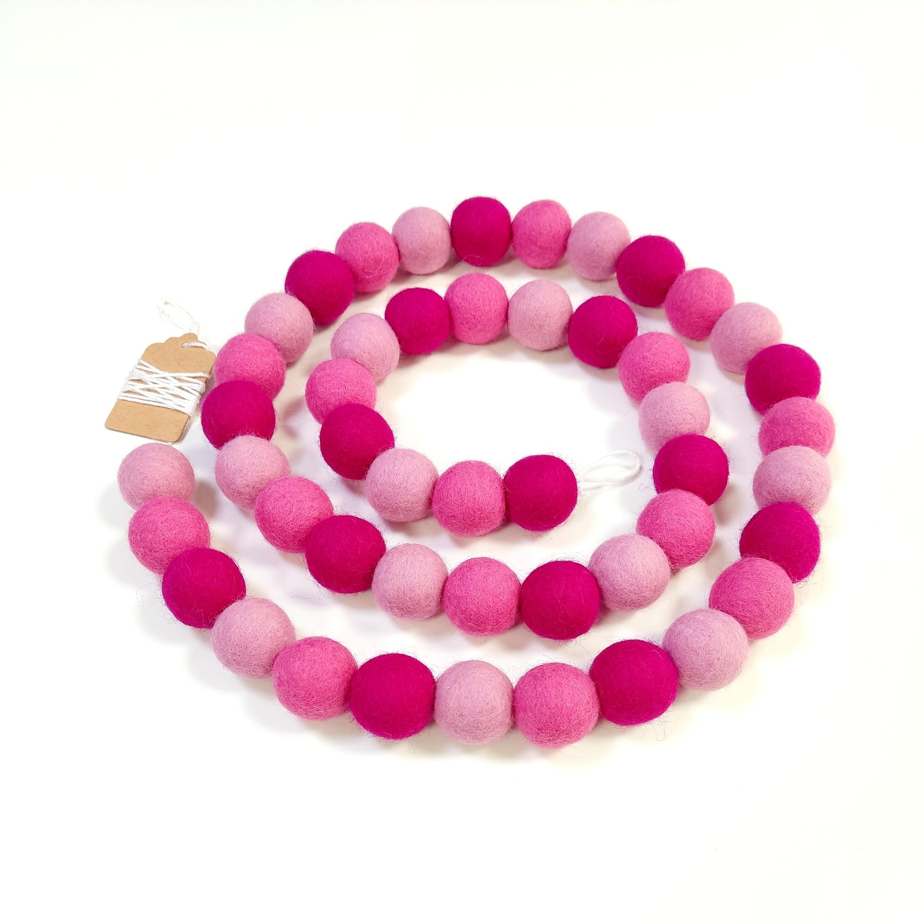 Guirlandes de pompons aux nuances roses vives et claires disposée en spirale sur une table