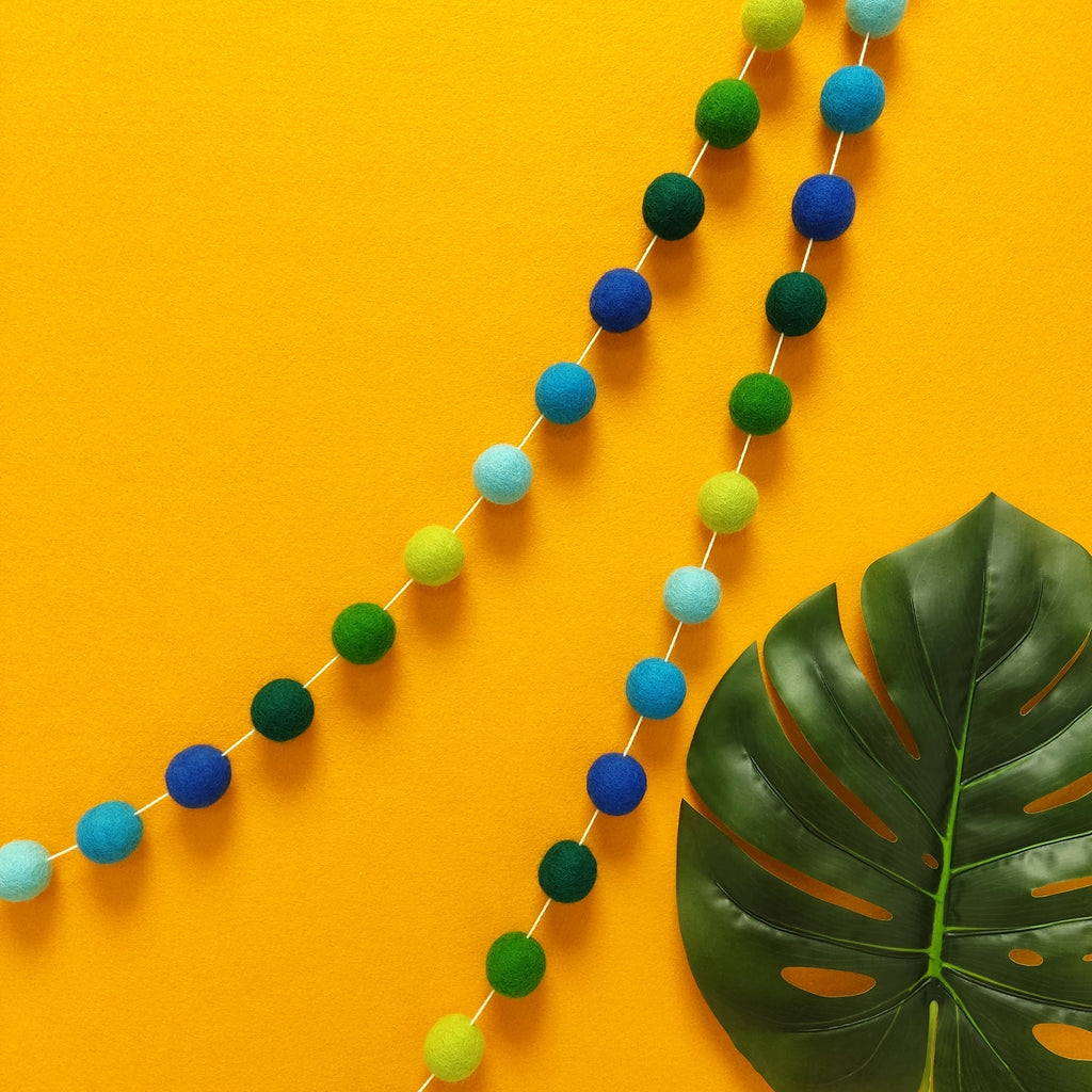 Guirlande de pompons feutrés aux teintes vertes et bleues suspendue sur un mur