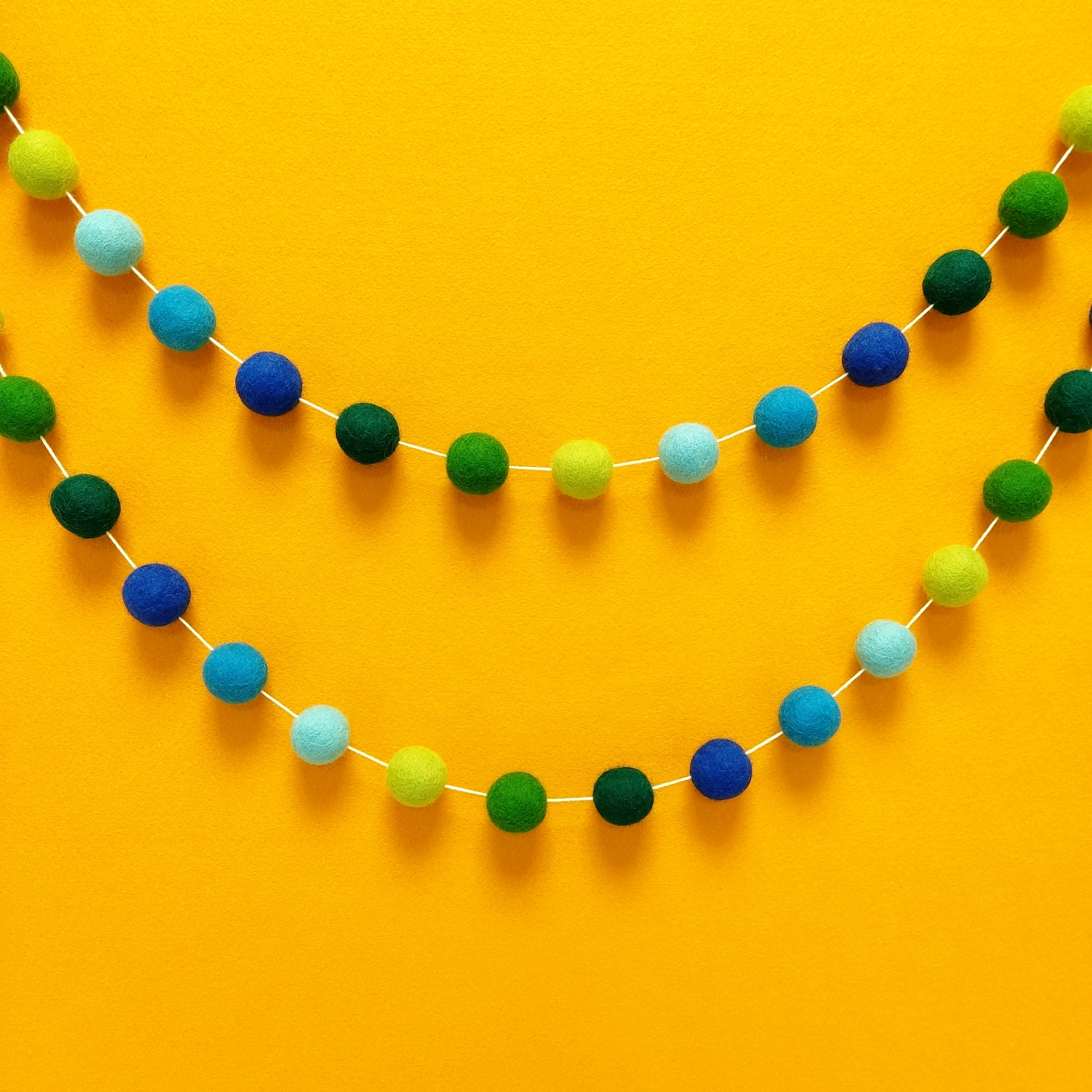 Guirlande boules de feutre bleu et vert tropicale fixée au mur en arc de cercle