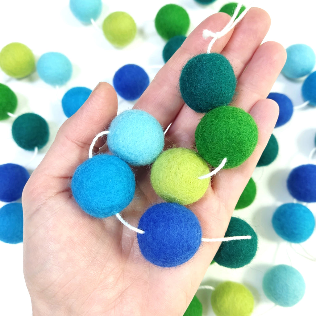 Détails des pompons en laine feutrée de 2,5 cm de la guirlande forêt tropicale dans une main