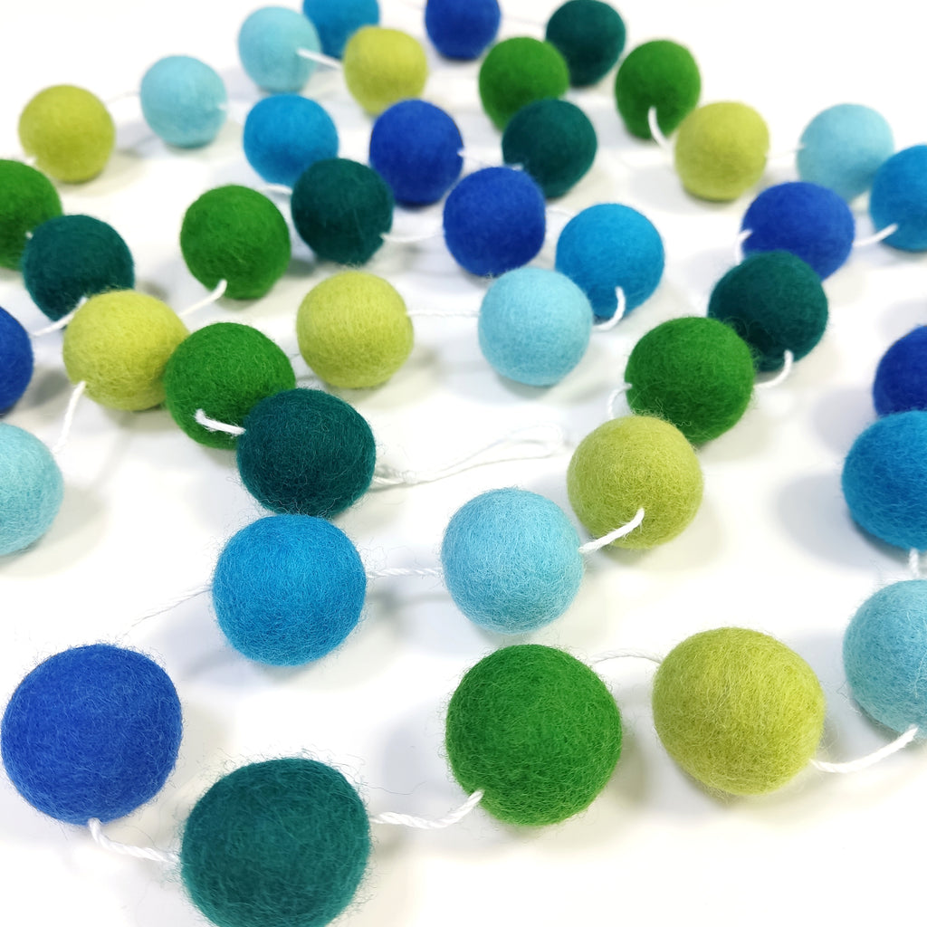 Guirlande en boules de laine feutrée forêt tropicale bleu et vert posée sur une table