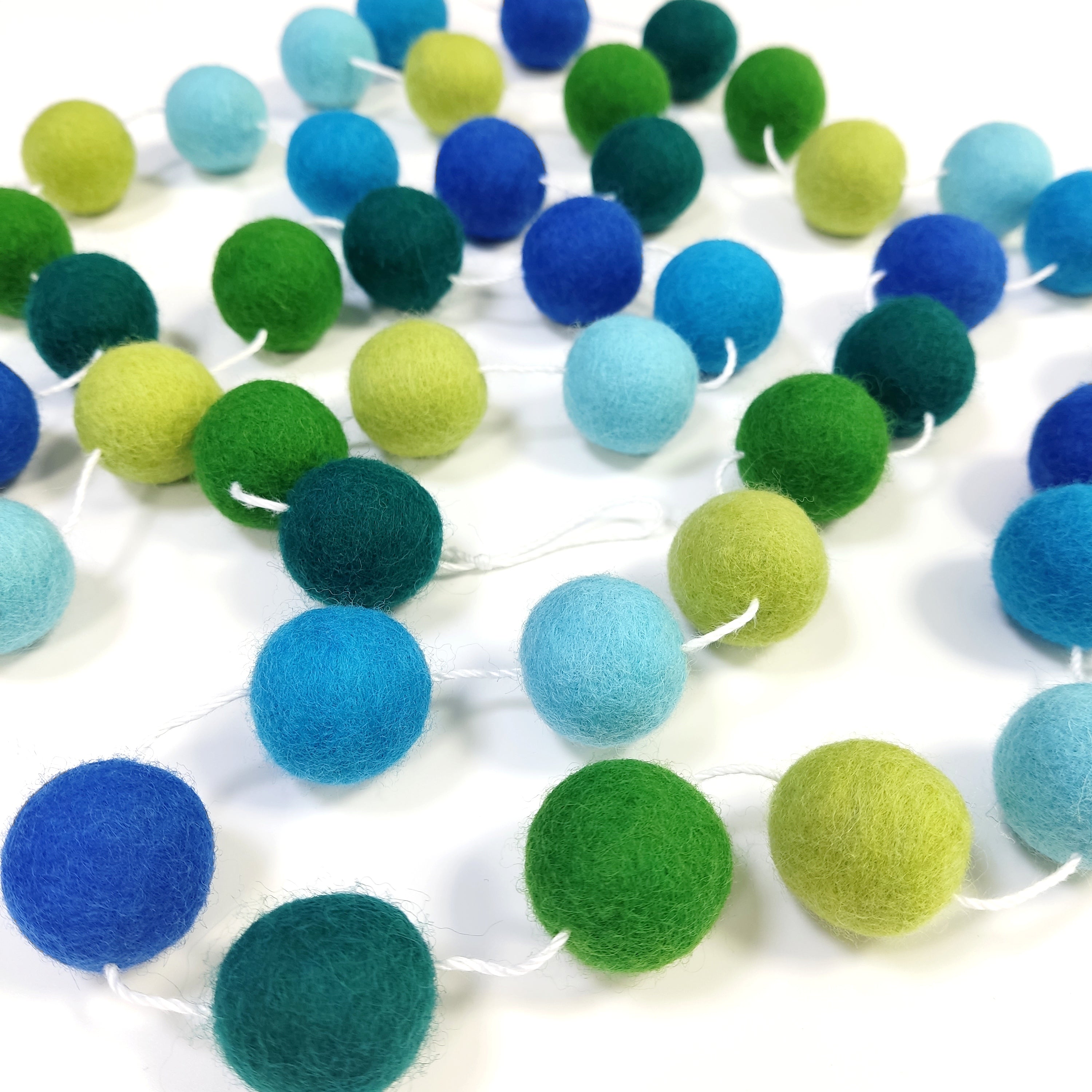 Guirlande en boules de laine feutrée forêt tropicale bleu et vert posée sur une table