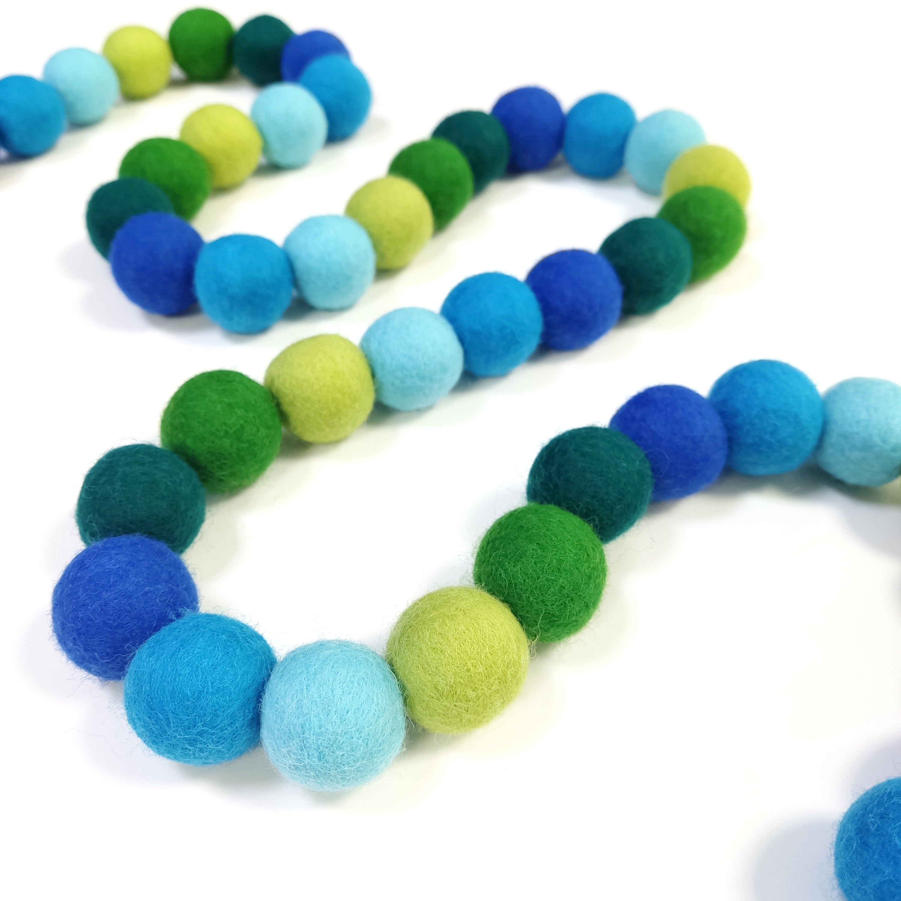 Guirlande de pompons vert et bleu disposée en serpentin sur une table