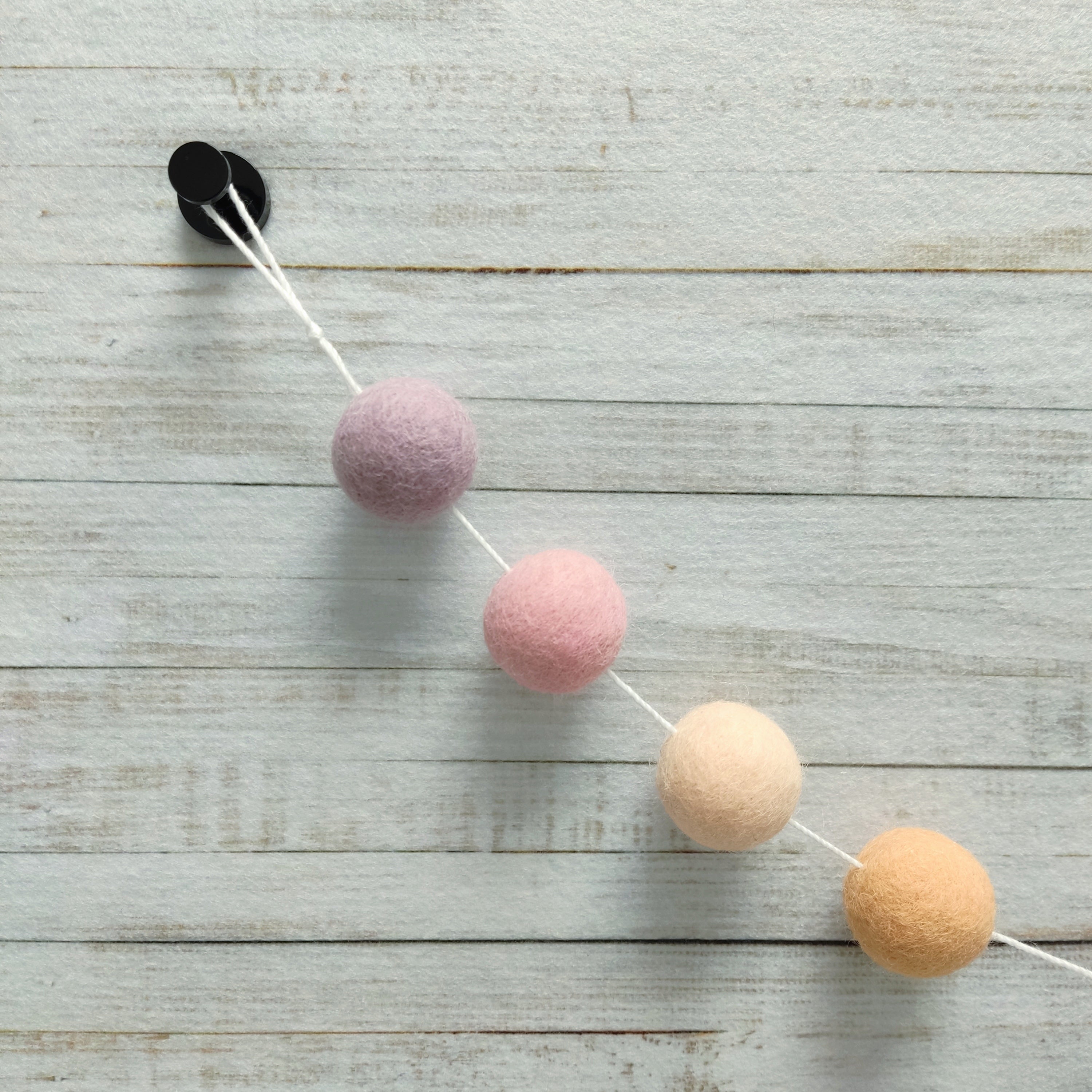 Zoom sur les pompons de la guirlande girly pêche, rose cerisier, lilas, orange et beige rosé