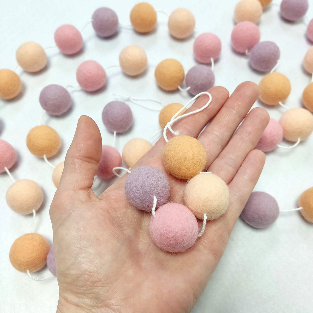 Détails des pompons de la guirlande rose pêche lilas de 2,5 cm dans une main