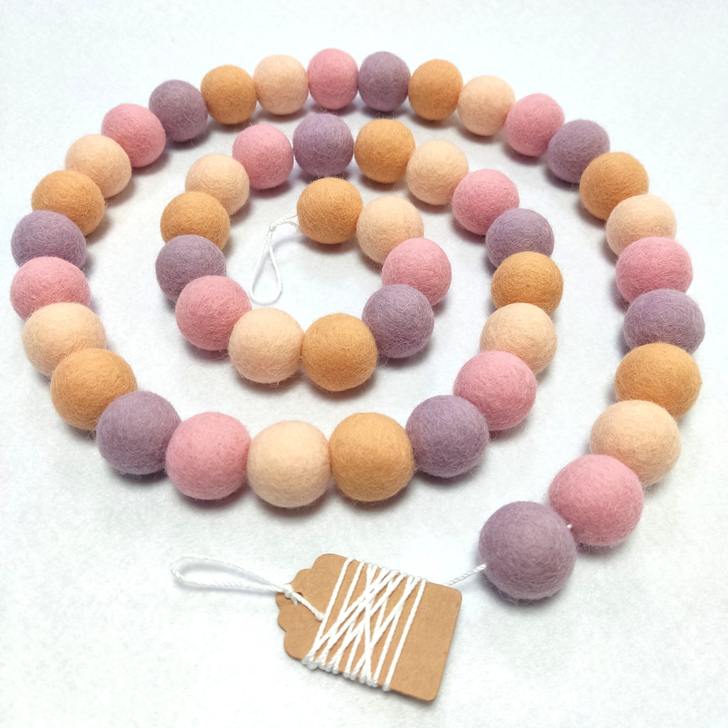 Guirlande de boules de feutres rose orange lilas disposée en spirale sur une table vue de dessus