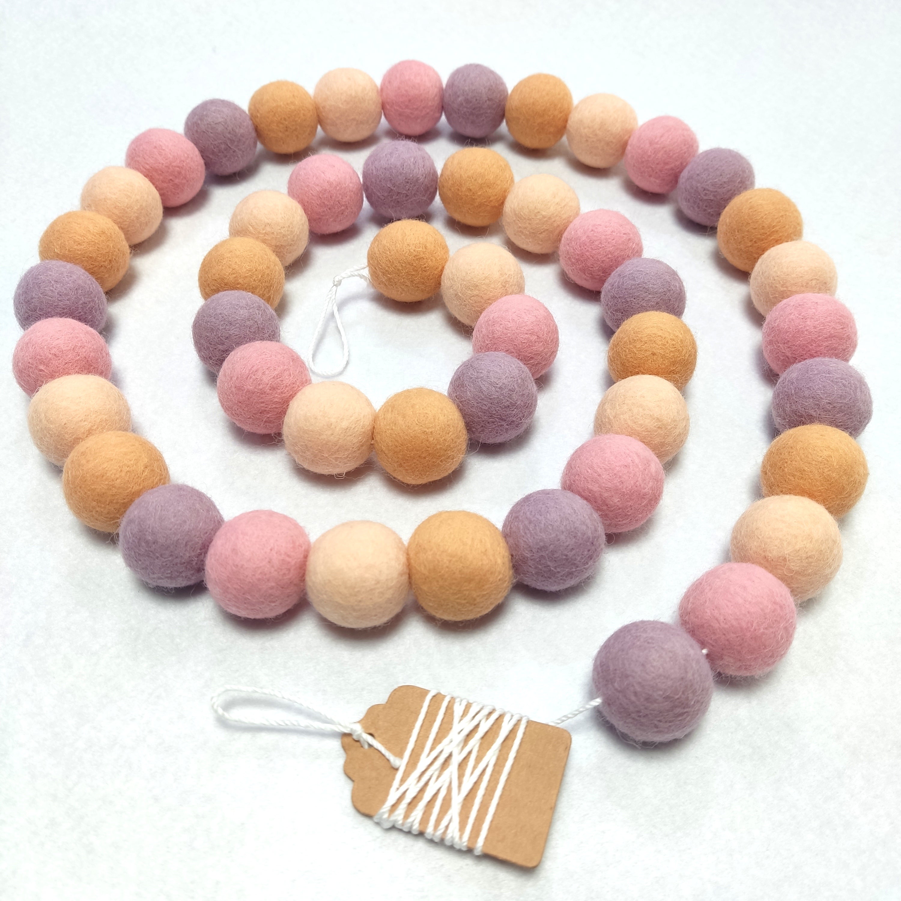 Guirlande de boules de feutres rose orange lilas disposée en spirale sur une table vue de dessus