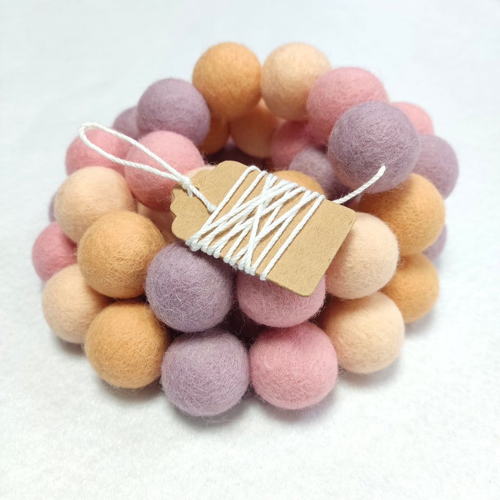Zoom sur la guirlande de pompons en feutre de laine mérinos girly pêche avec étiquette