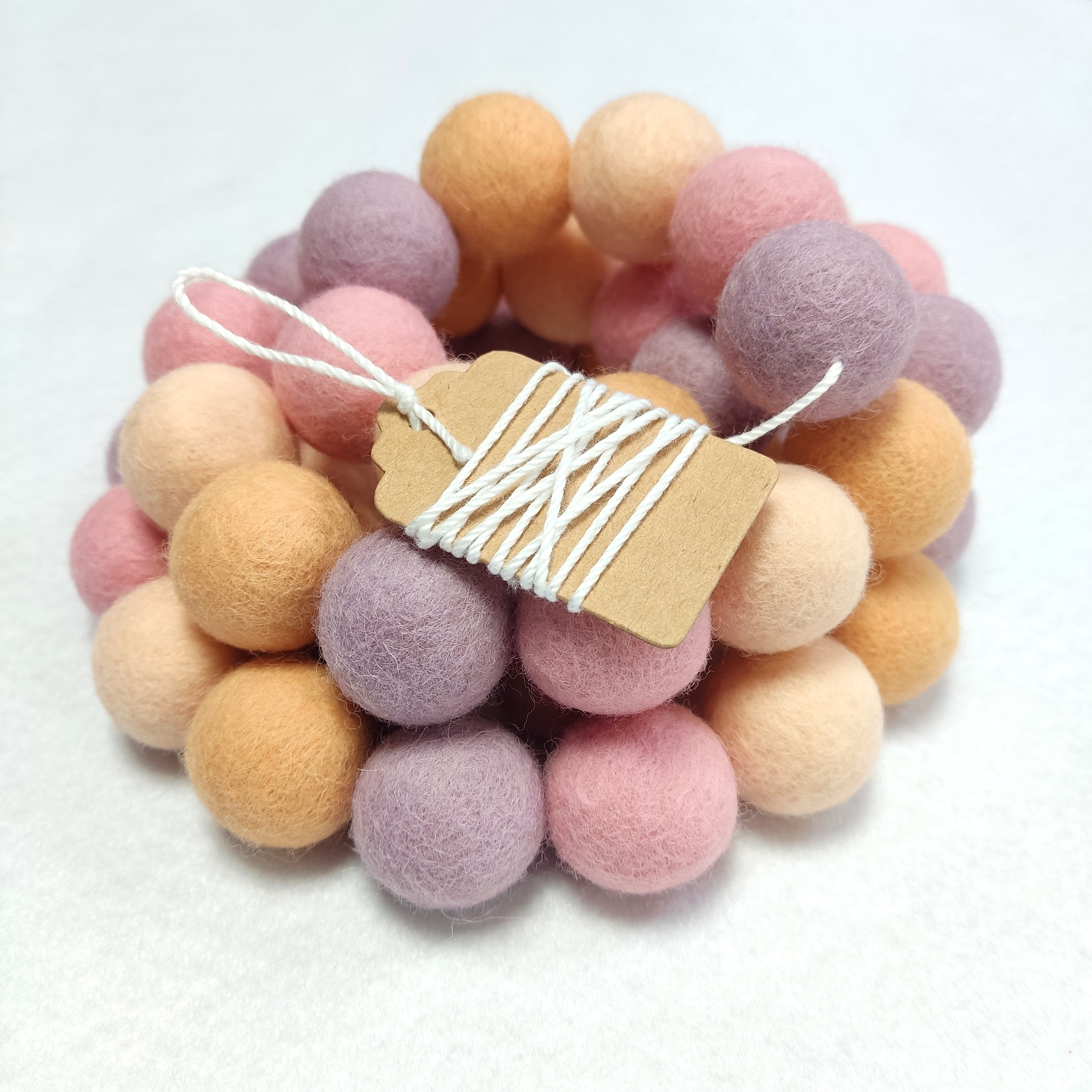 Zoom sur la guirlande de pompons en feutre de laine mérinos girly pêche avec étiquette
