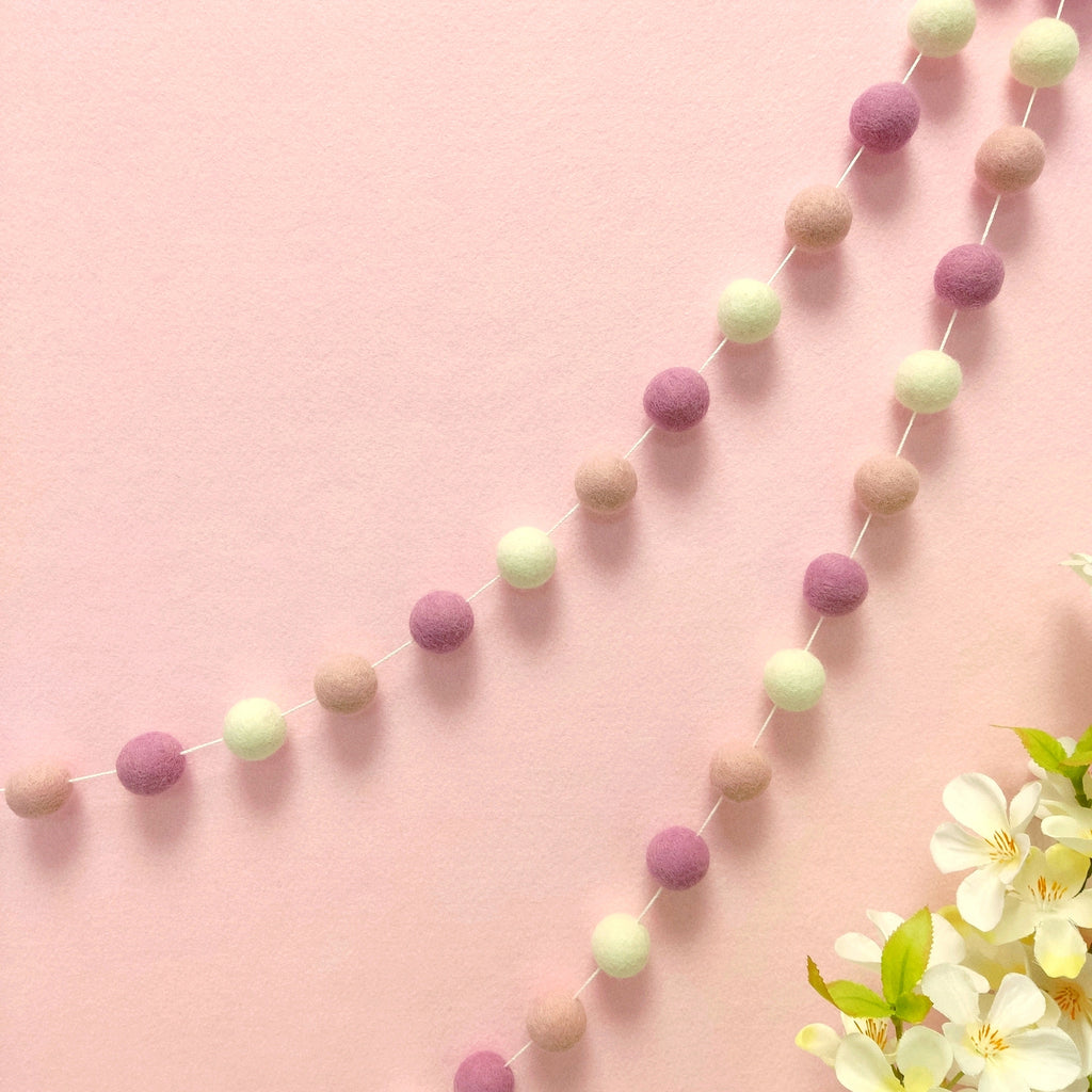 Guirlande de pompons feutrés guimauve rose blanc naturel rose poudré suspendue sur un mur