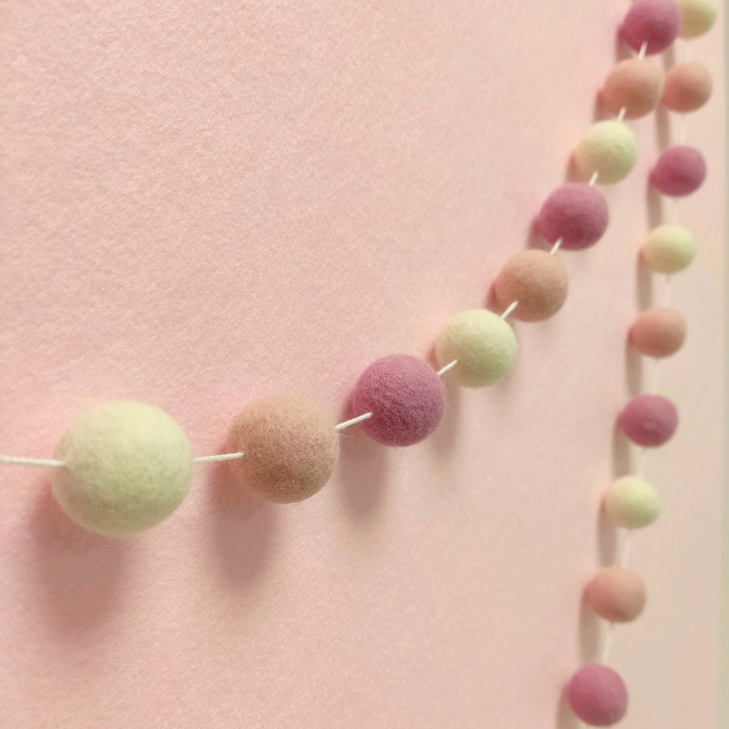 Guirlande de pompons guimauve rose vue de profil sur un mur de chambre bébé
