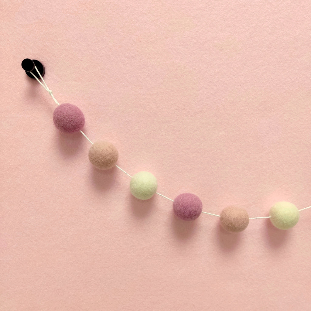 Zoom sur les pompons de laine mérinos blanc naturel, rose poudré et rose cerisier de la guirlande guimauve rose