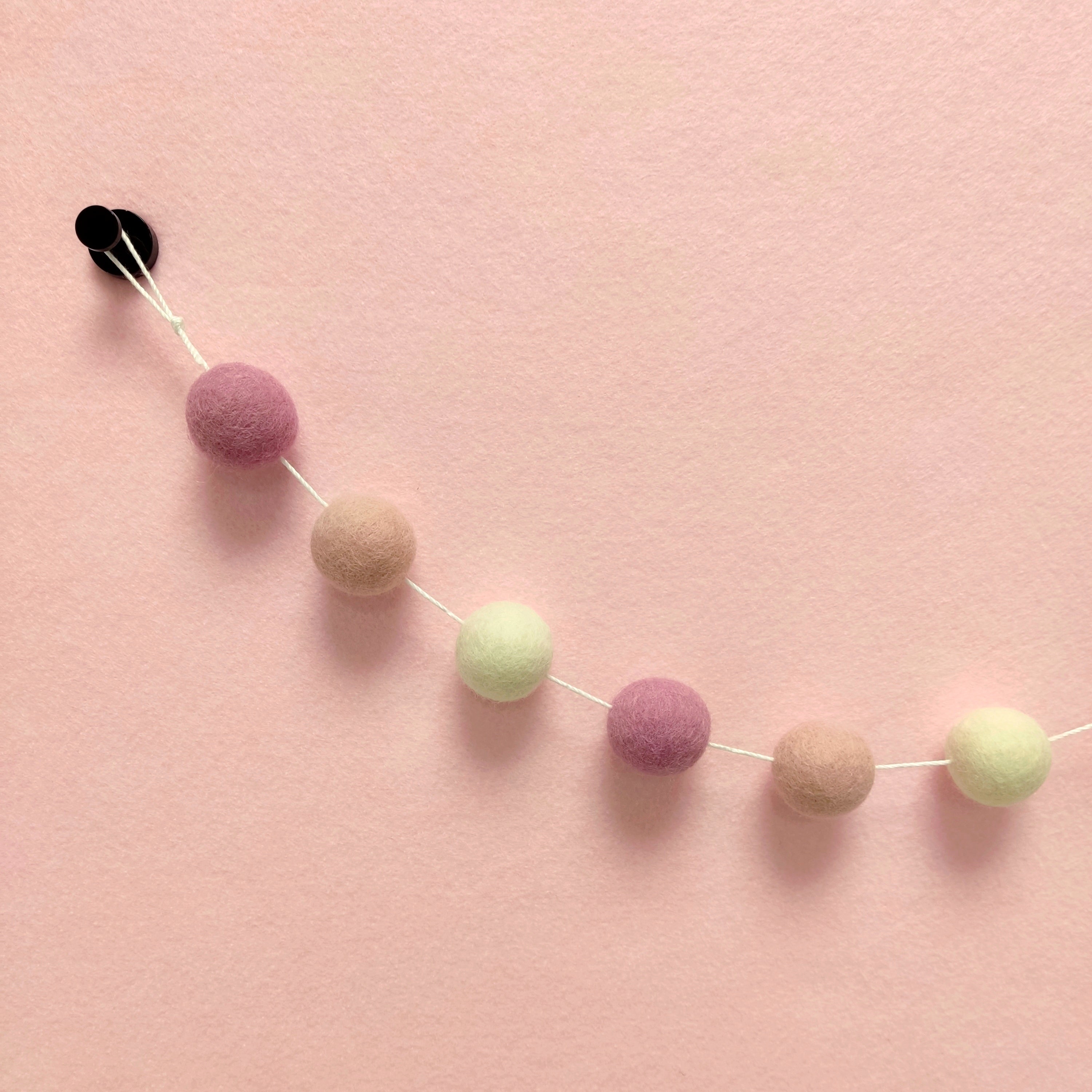 Zoom sur les pompons de laine mérinos blanc naturel, rose poudré et rose cerisier de la guirlande guimauve rose