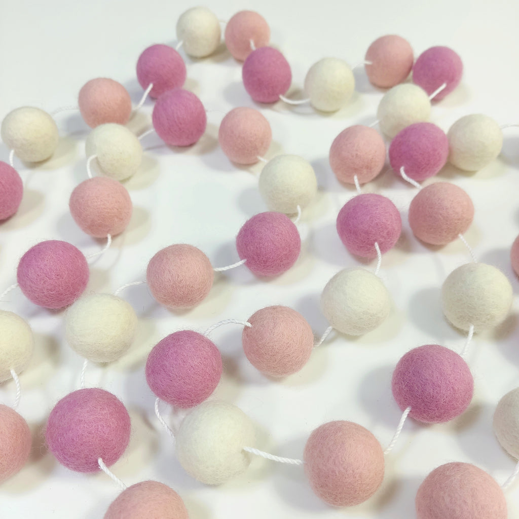 Guirlande de pompons guimauve rose étalée sur une table avec les pompons espacés
