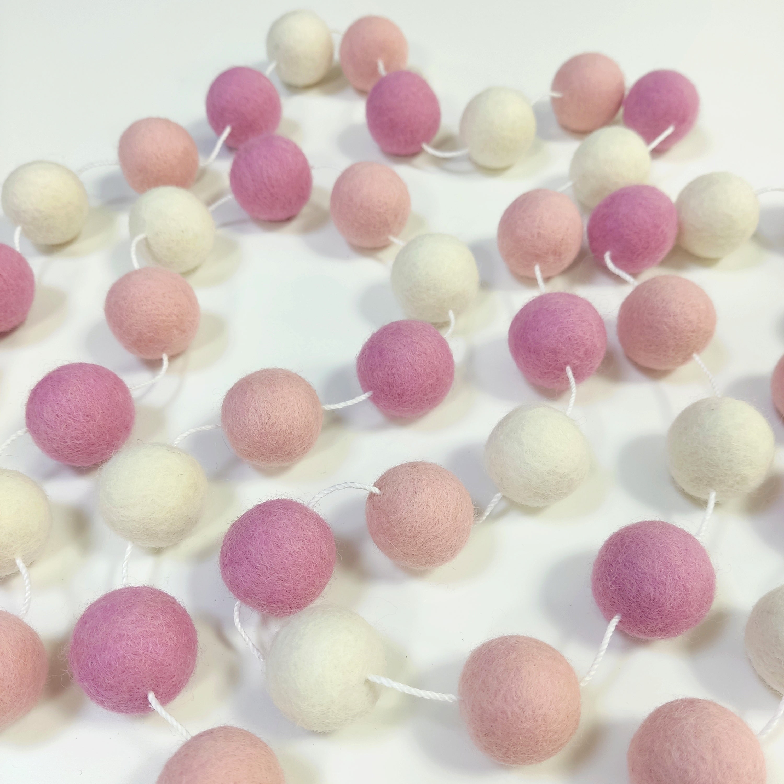 Guirlande de pompons guimauve rose étalée sur une table avec les pompons espacés