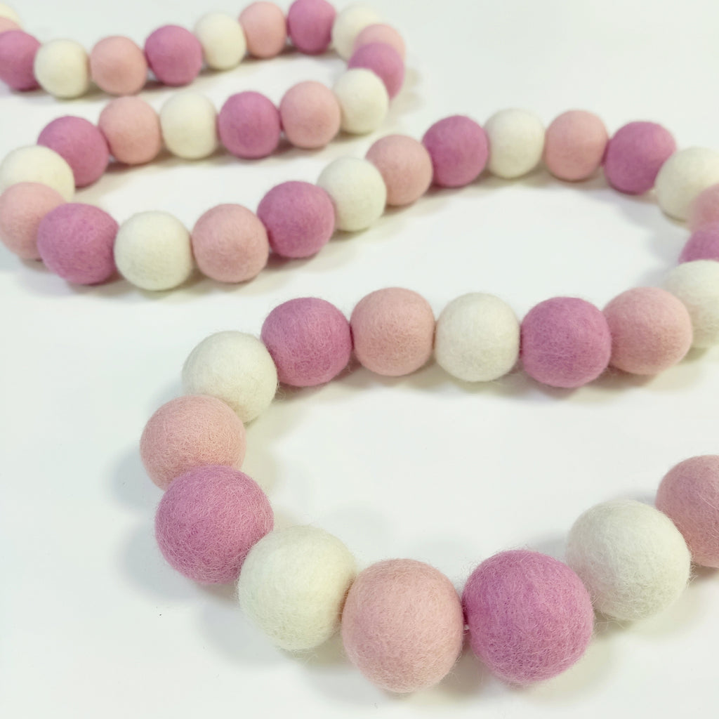 Guirlande en boules de feutre guimauve rose disposée en serpentin sur une table