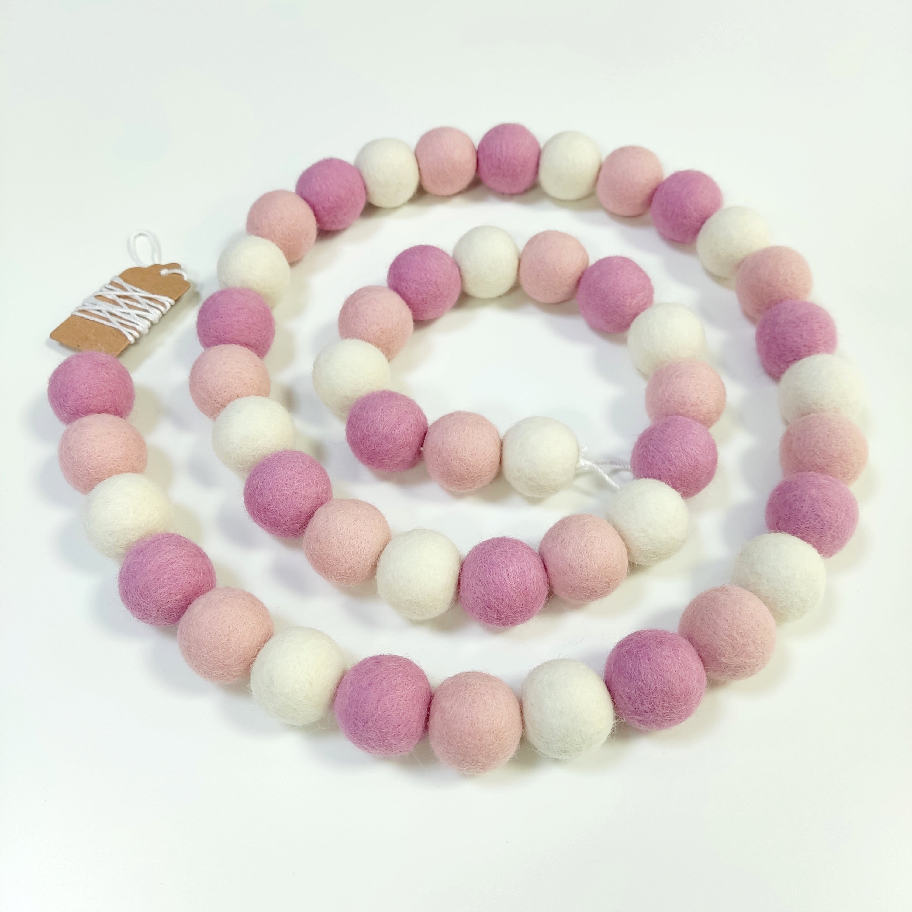 Guirlande de pompons guimauve rose disposée en spirale sur une table