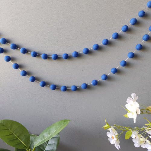 Guirlande de pompons en laine feutrée bleu indigo suspendue sur un mur vue de loin