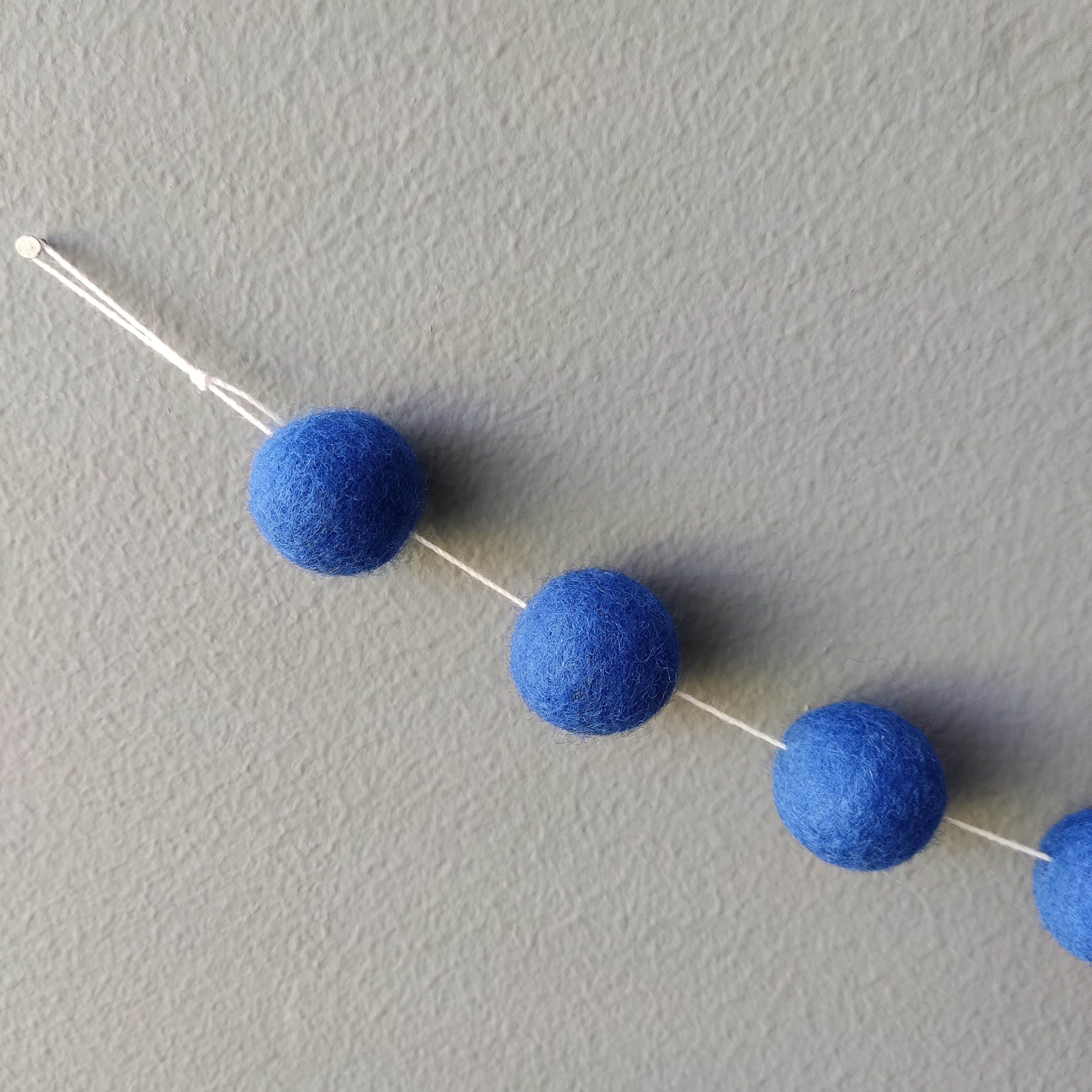 Zoom sur les pompons bleu indigo de la guirlande en boules de feutre avec la boucle de fixation