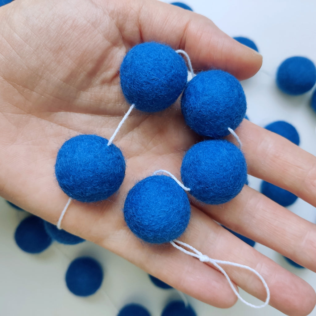 Détail des pompons de feutres bleu indigo de la guirlande dans une main