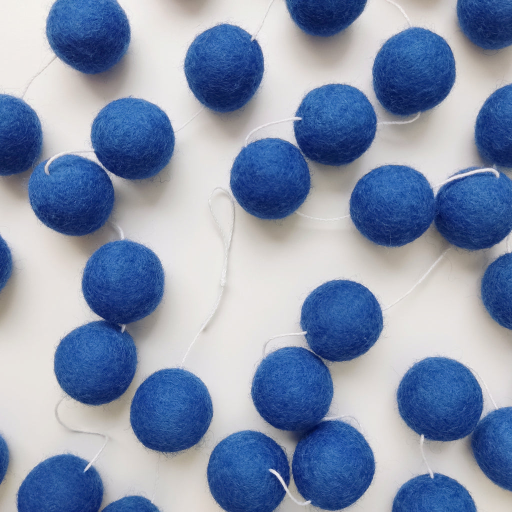 Guirlande de boules laine feutrée bleu indigo posée sur une table avec les pompons espacés