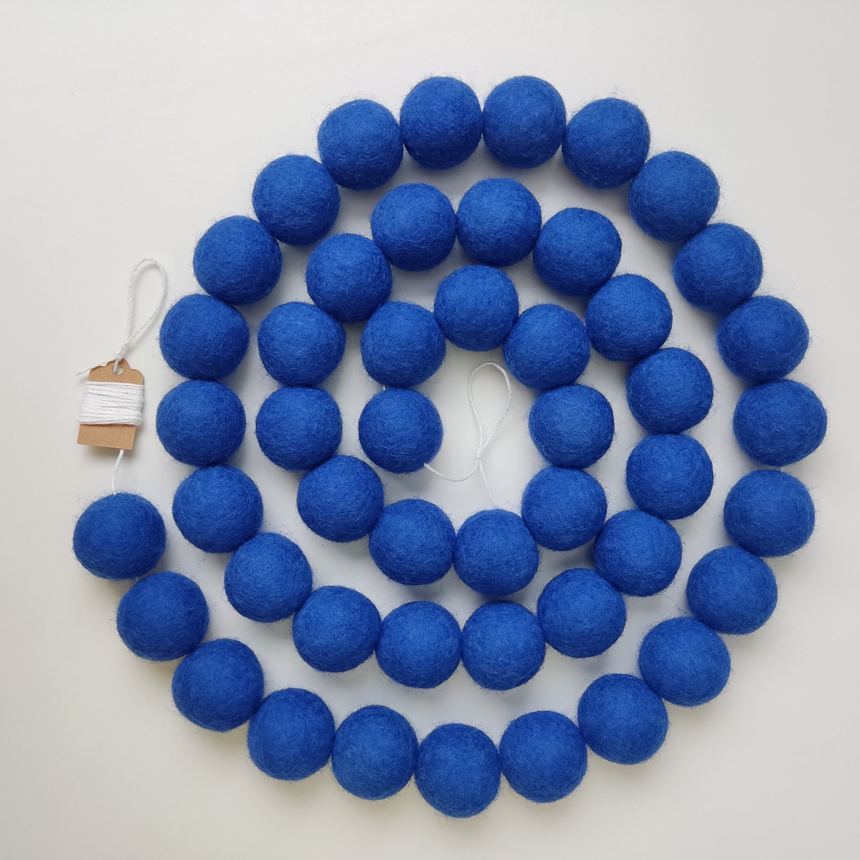 Guirlande de pompons bleu indigo posée en spirale avec les pompons rassemblés sur le fil vue de dessus