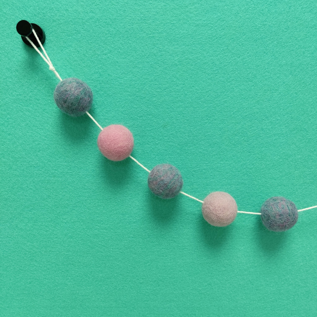 Détail des pompons feutrés lilas, rose cerisier et mélange turquoise rose lilas de la guirlande Jardin de Lilas