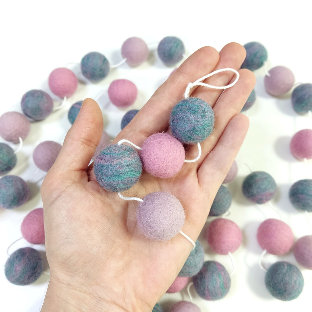 Zoom sur les pompons en laine mérinos jardin de lilas dans une main, teintes florales et romantiques