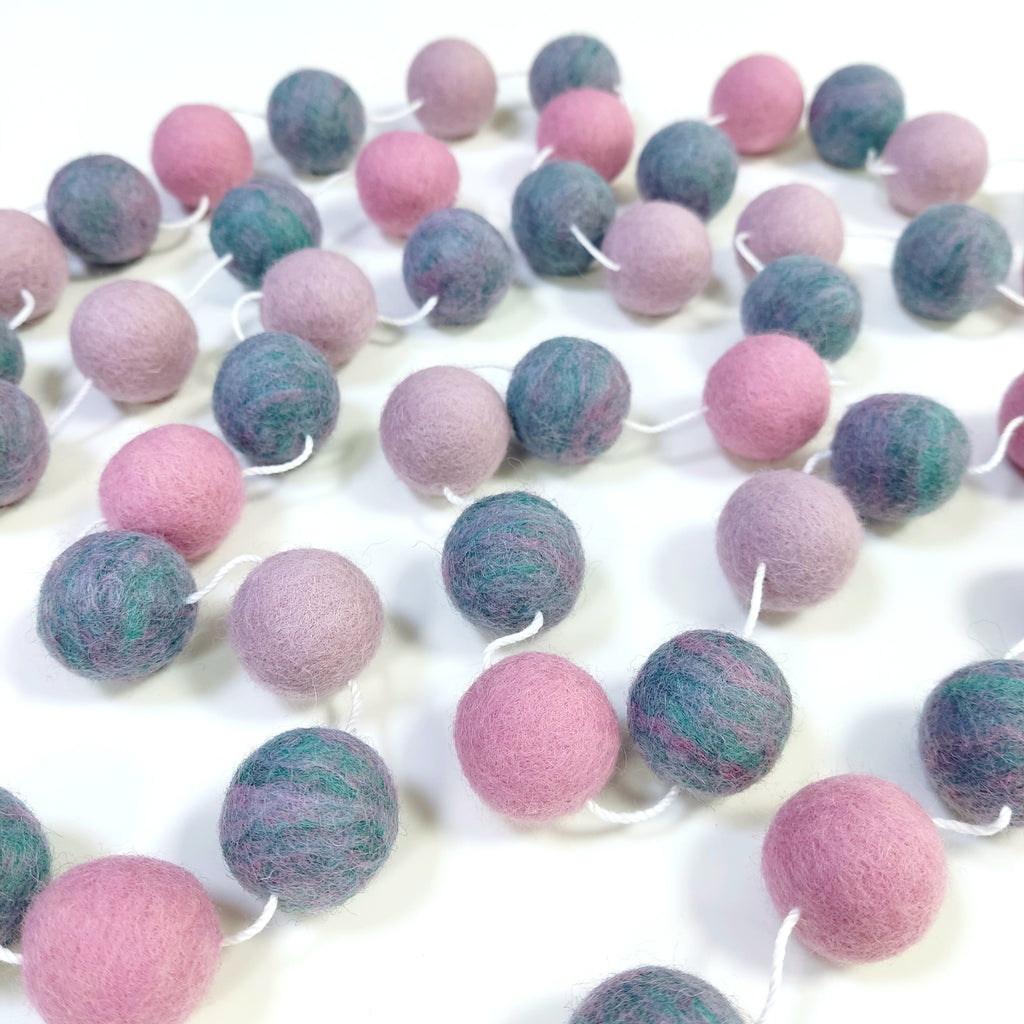 Guirlande de pompons feutrés jardin de lilas étalée sur une table avec les pompons espacés sur le fil