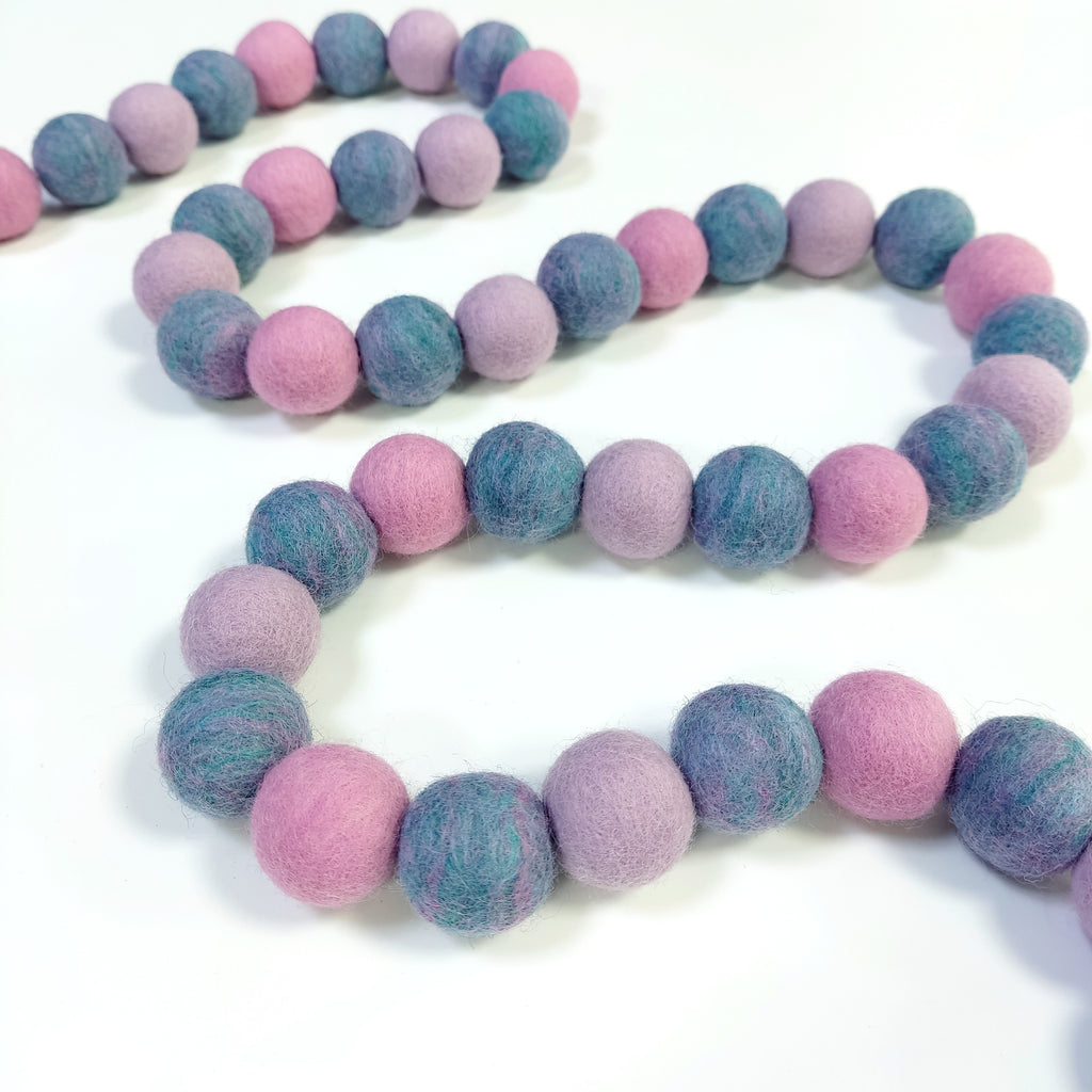 Guirlande en boules de feutre jardin de lilas disposée en serpentin sur une table