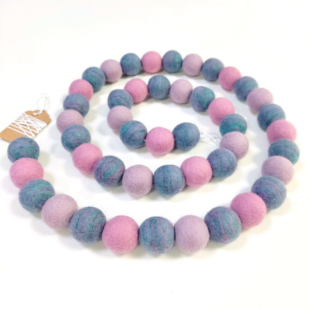 Guirlande de pompons feutrés jardin de lilas disposée en spirale sur fond blanc