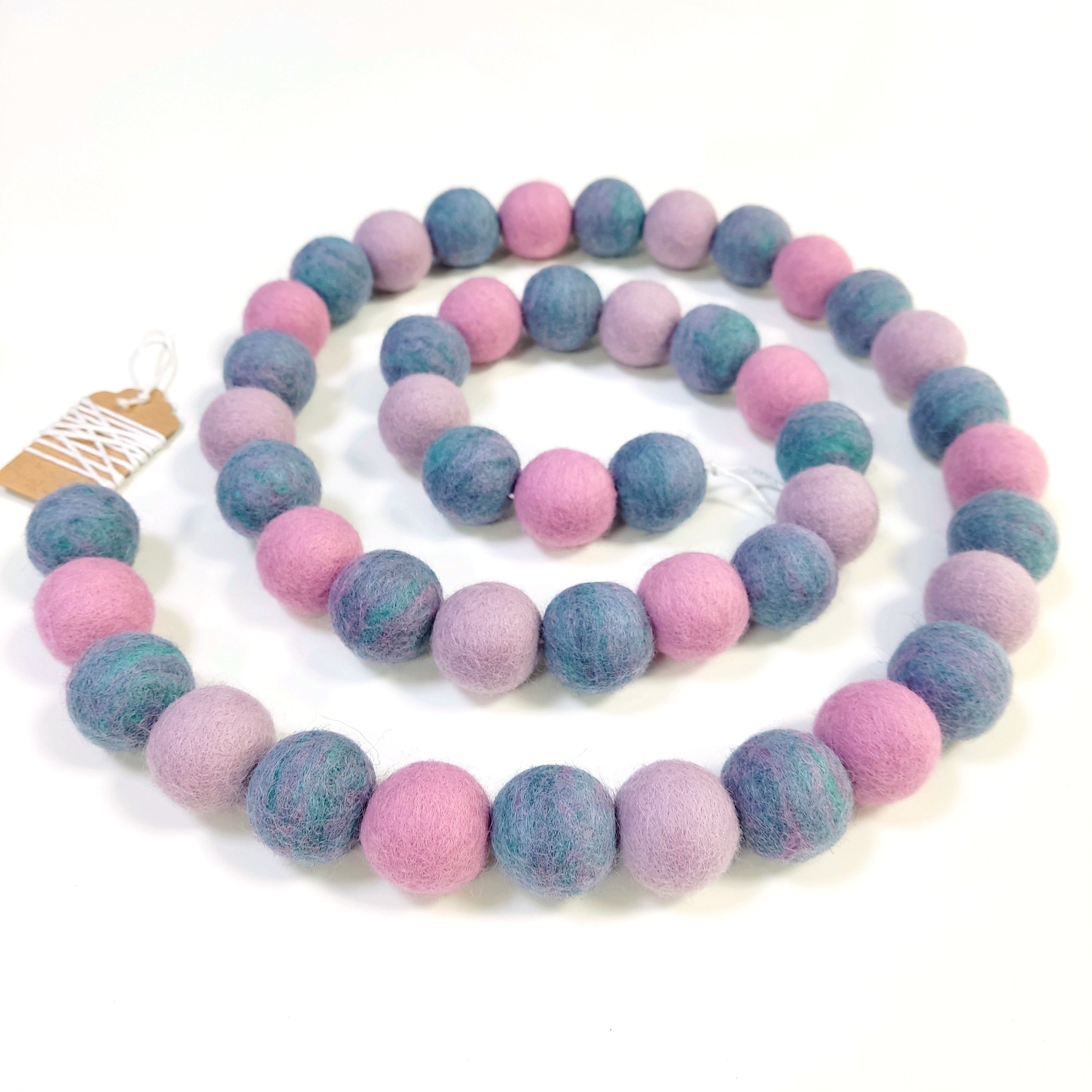 Guirlande de pompons feutrés jardin de lilas disposée en spirale sur fond blanc