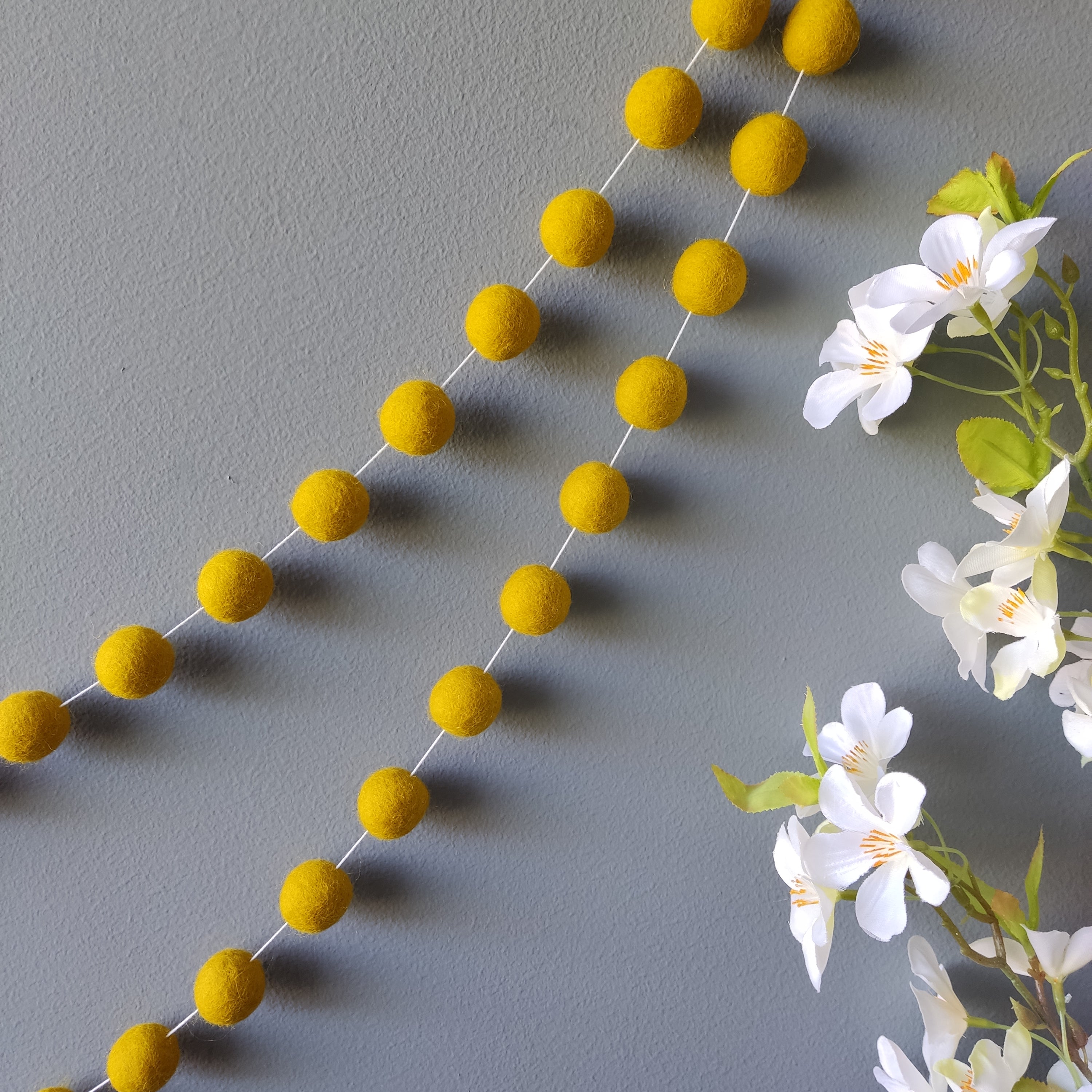 Guirlande de pompons jaune moutarde suspendue sur un mur