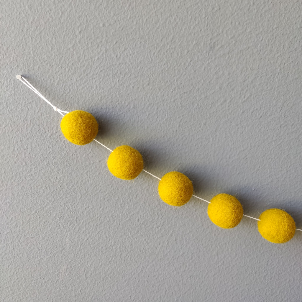 Zoom sur les pompons jaune moutarde et la boucle de fixation de la guirlande