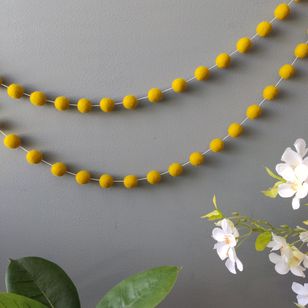 Guirlande en boules de feutre jaune moutarde fixée au mur vue de loin