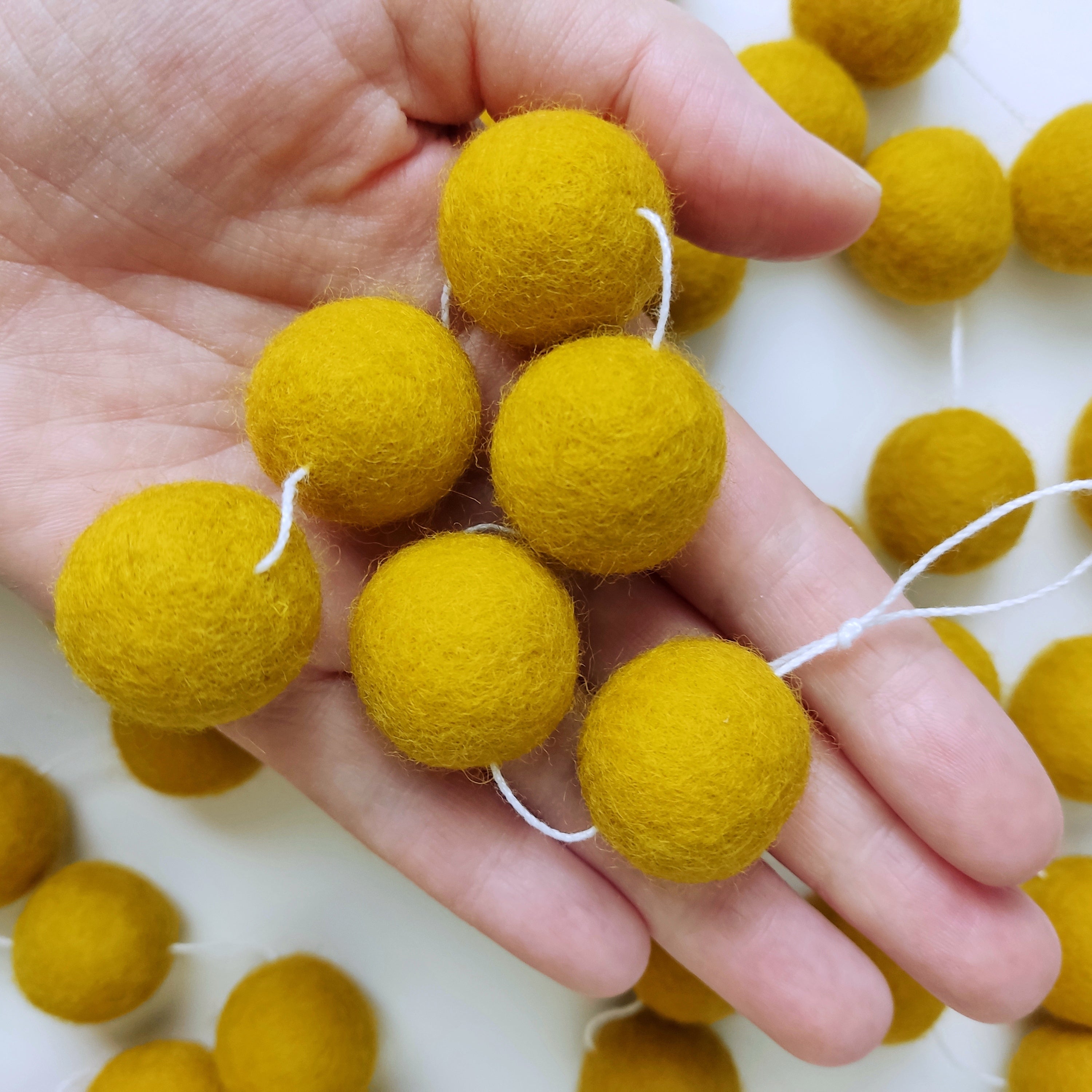 Détails des pompons feutrés jaune moutarde de 2,5 cm dans une main