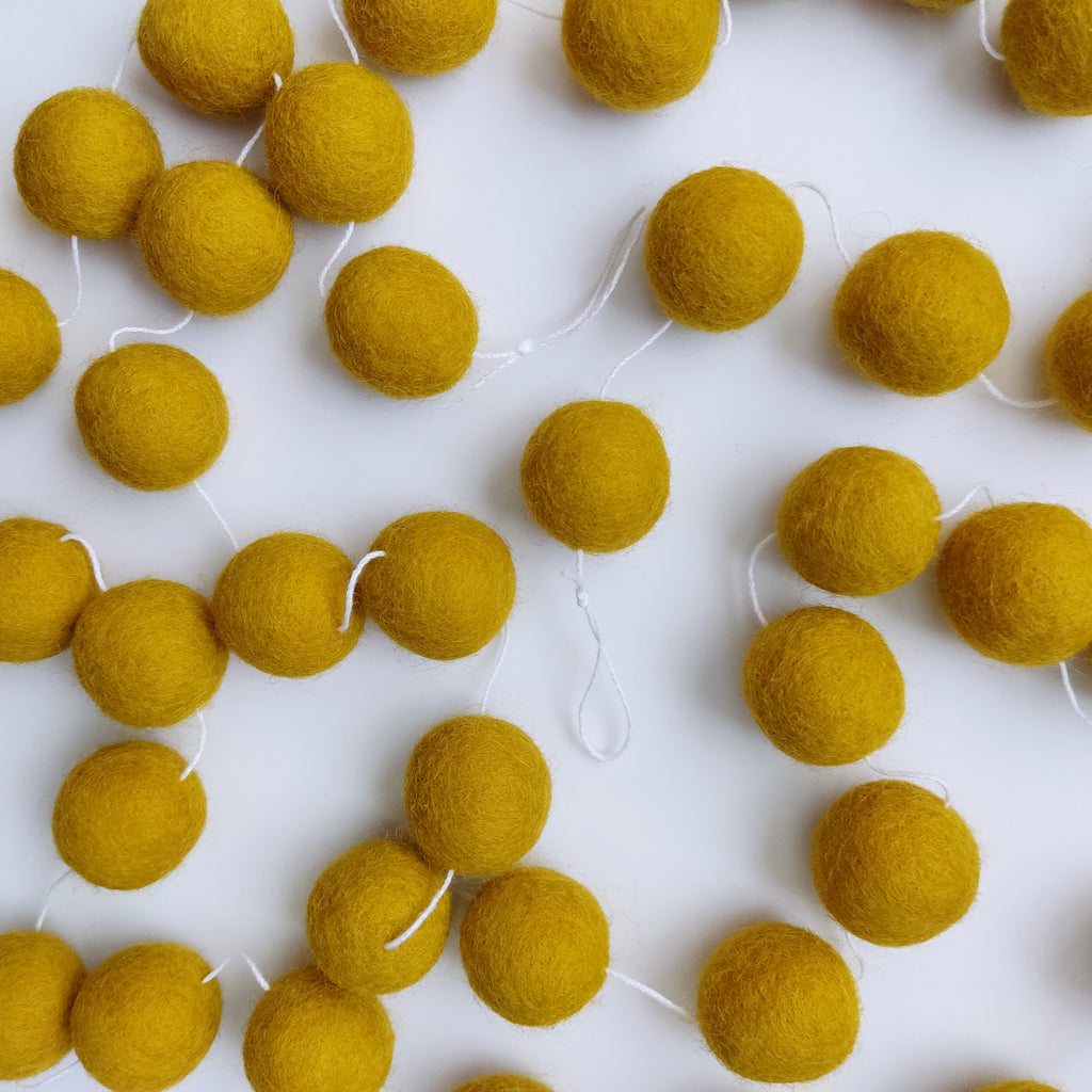 Guirlande jaune moutarde en pompons de laine feutrée posée sur une table