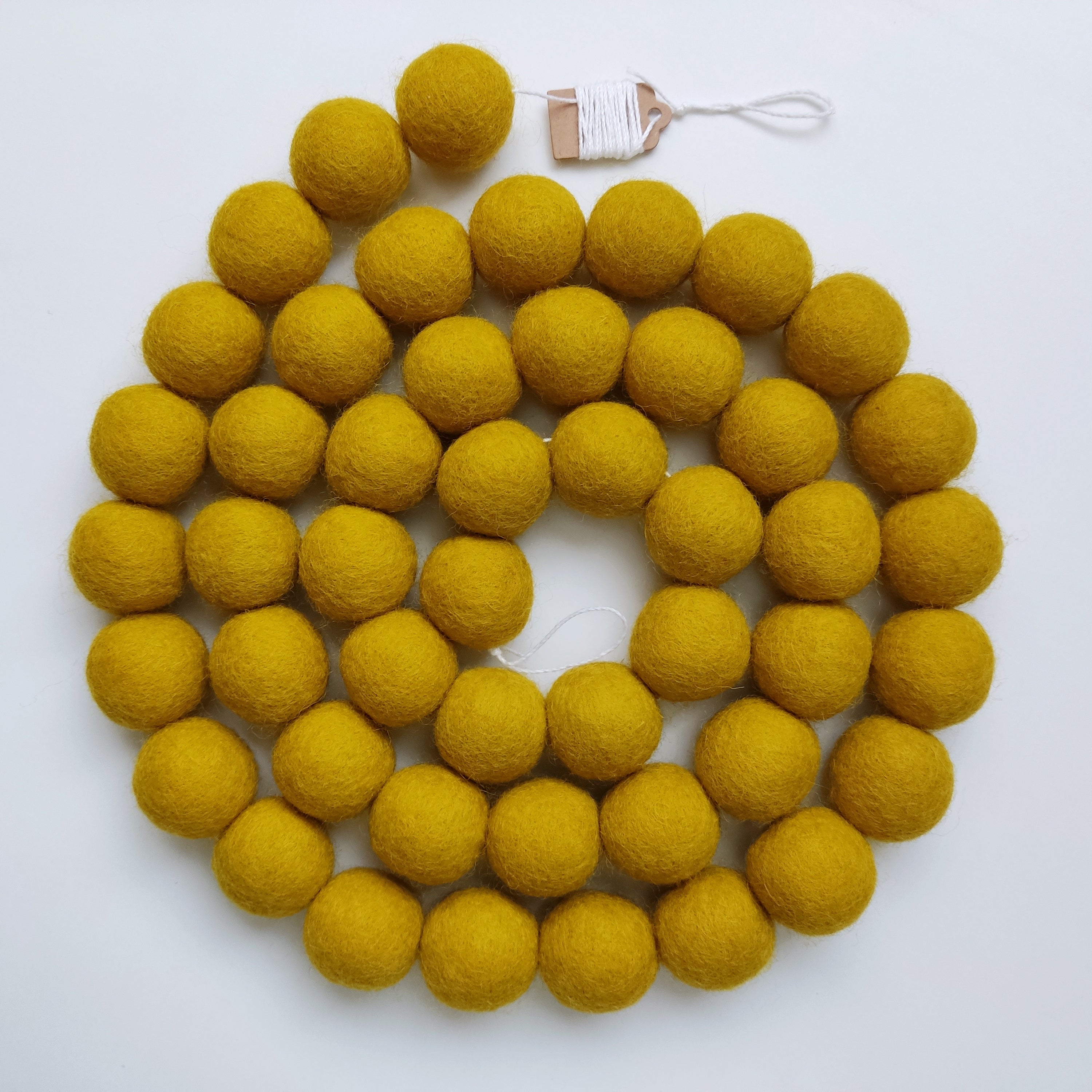 Guirlande de pompons en laine feutrée jaune moutarde positionnée en spirale vue de dessus