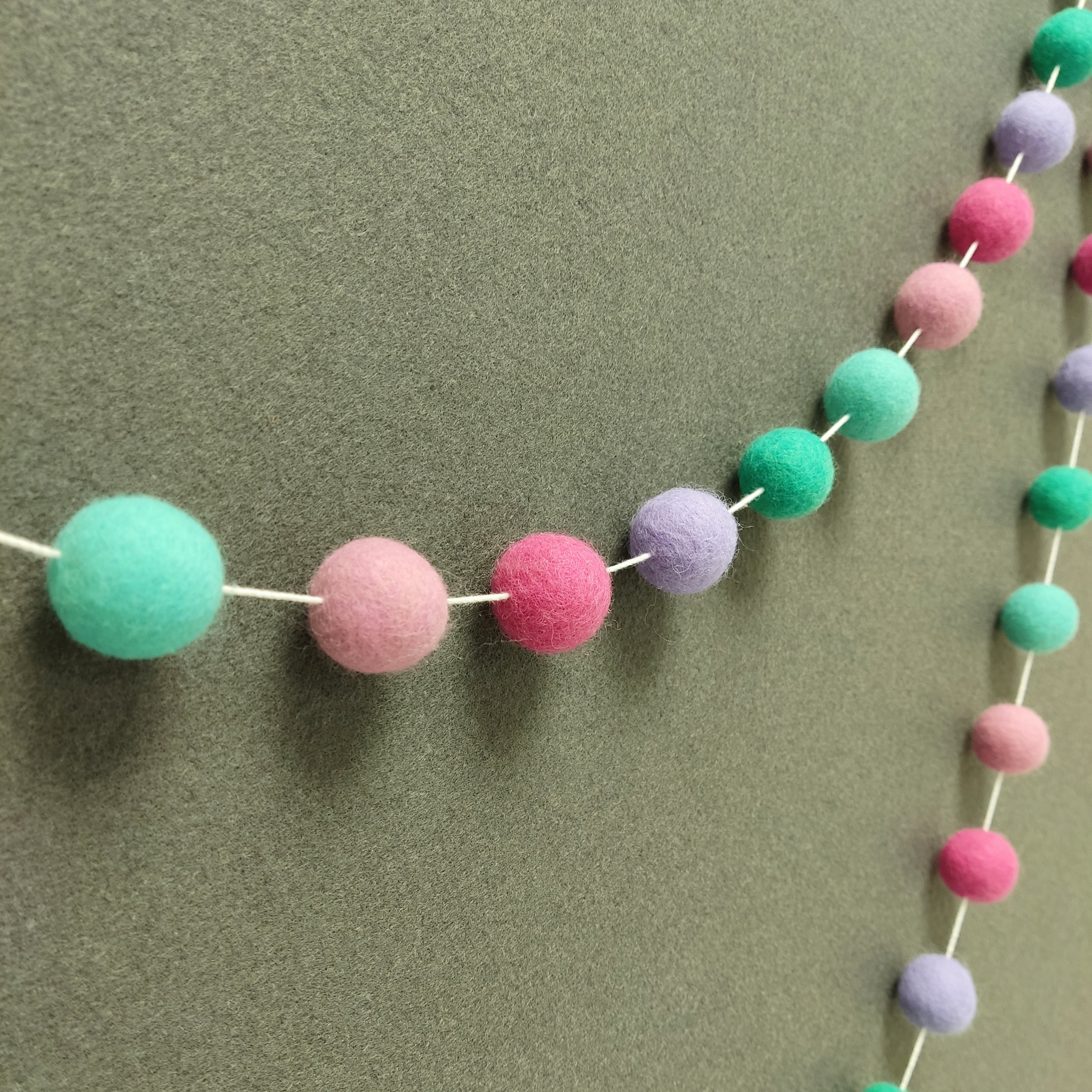 Guirlande de pompons feutrés aux teintes féeriques turquoise, lagon, lavande et rose vue de profil