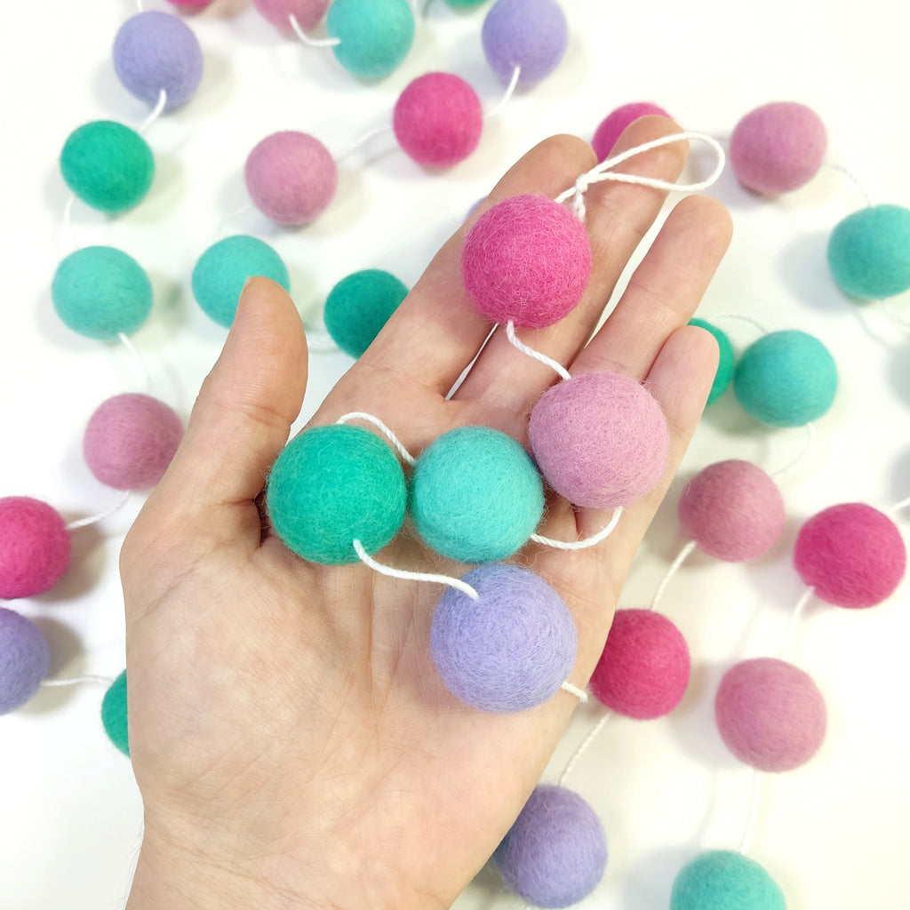 Zoom sur les pompons en laine mérinos lagon rose dans une main, teintes aquatiques et roses