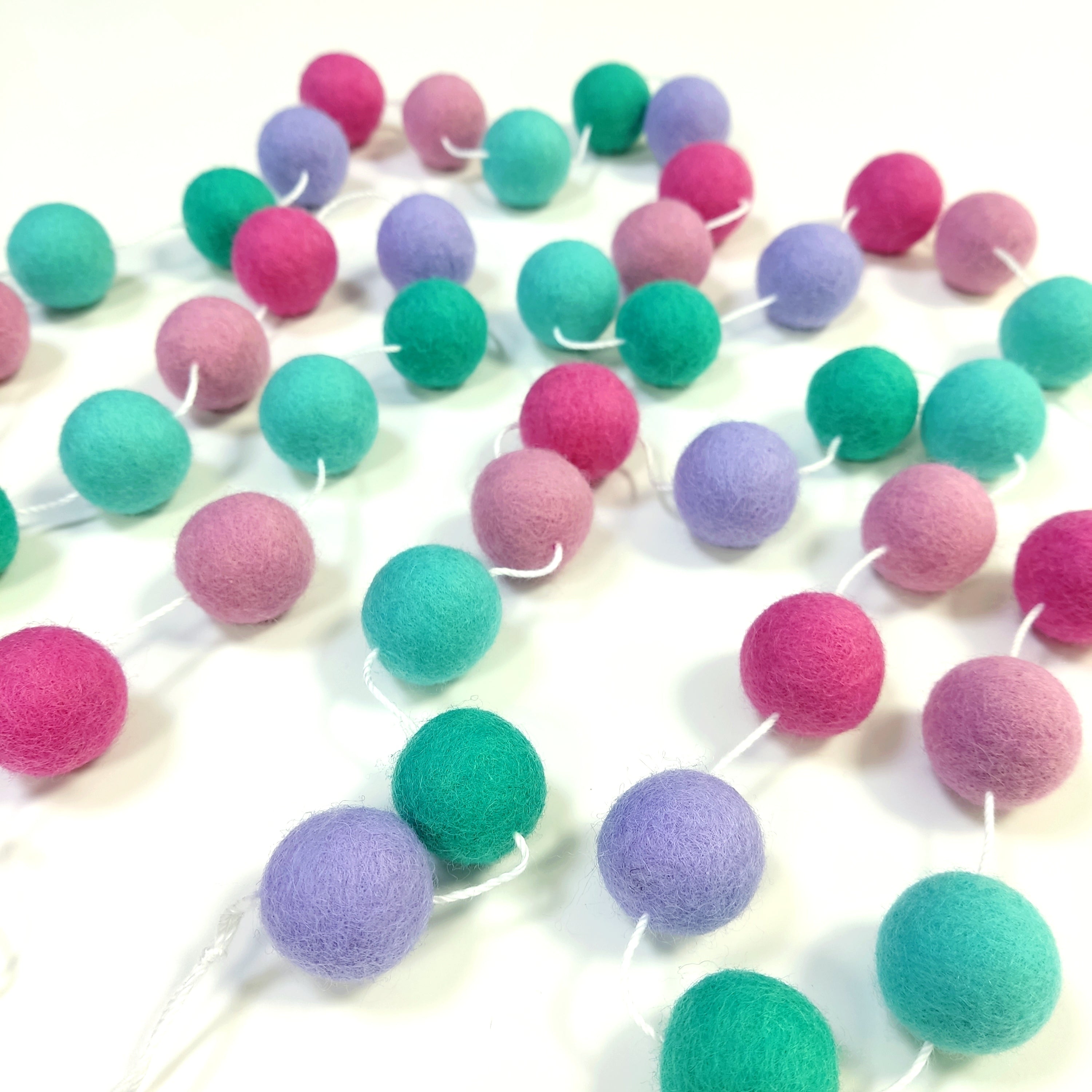 Guirlande de pompons feutrés lagon rose étalée sur une table avec les pompons espacés sur le fil