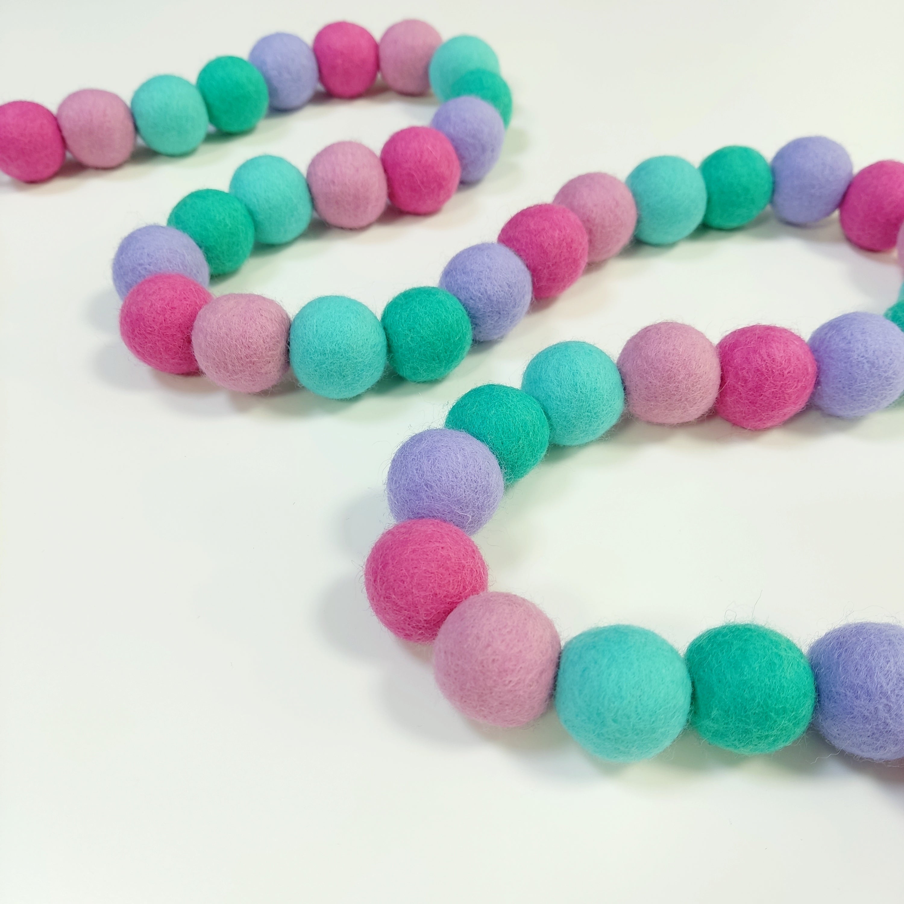 Guirlande en boules de feutre lagon rose disposée en serpentin sur une table