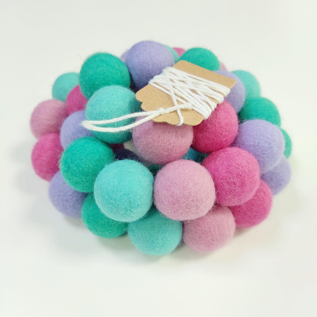 Zoom sur la guirlande de pompons en laine mérinos lagon rose avec étiquette CELAINEDECO