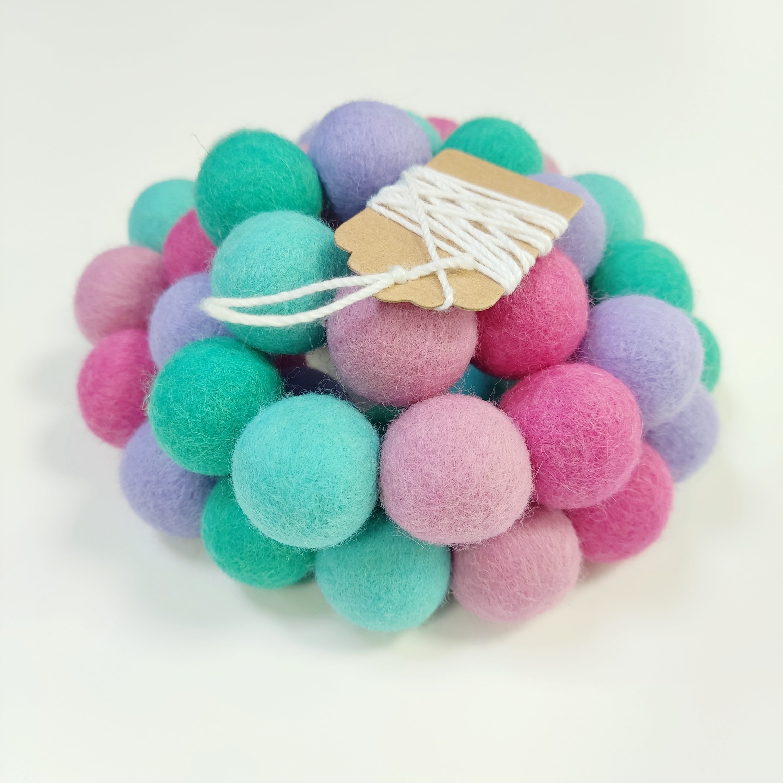 Zoom sur la guirlande de pompons en laine mérinos lagon rose avec étiquette CELAINEDECO