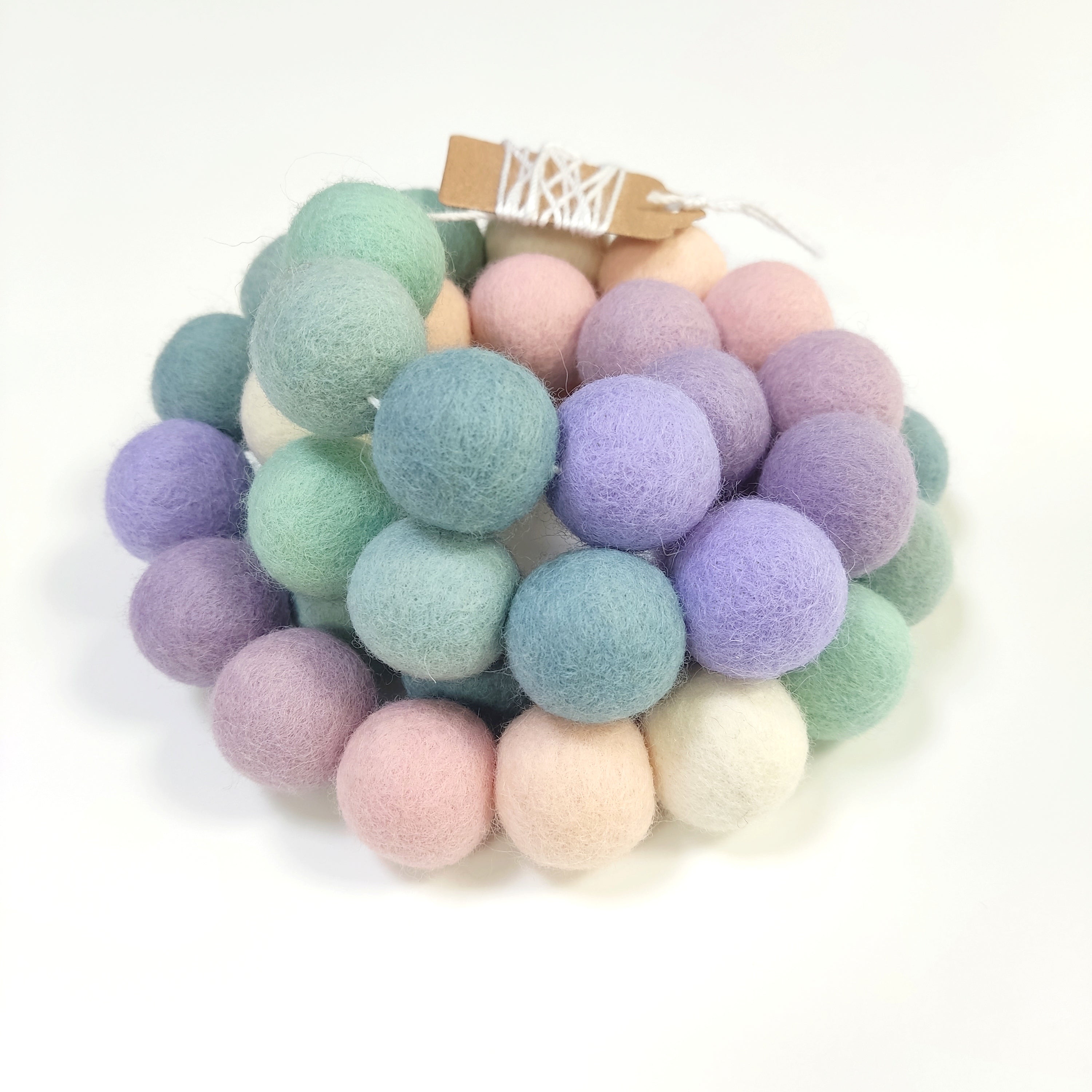 Zoom sur la guirlande de pompons en laine mérinos lavande sauge avec étiquette CELAINEDECO