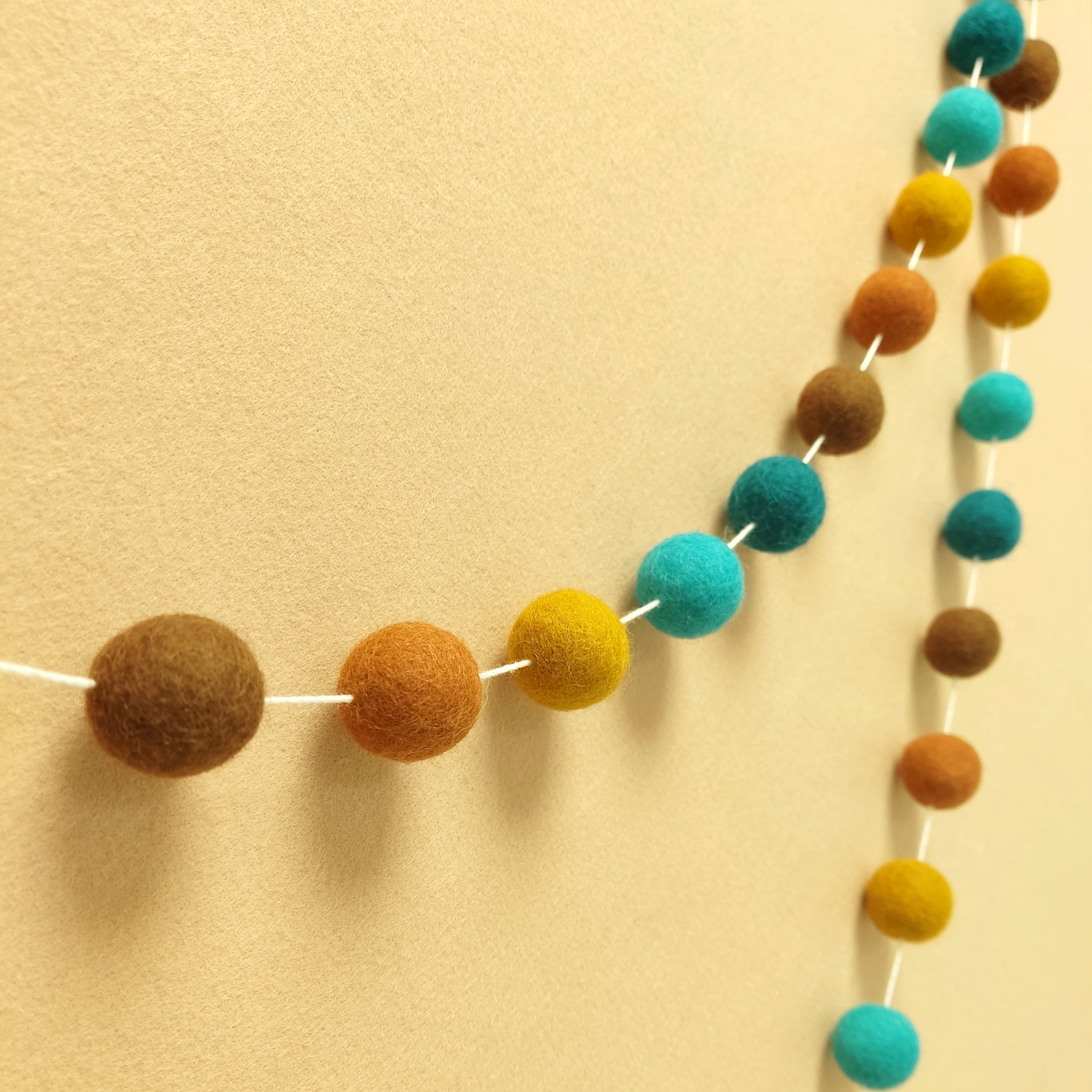Guirlande de pompons feutrés aux teintes orientales terracotta, ocre, turquoise et vert canard vue de profil