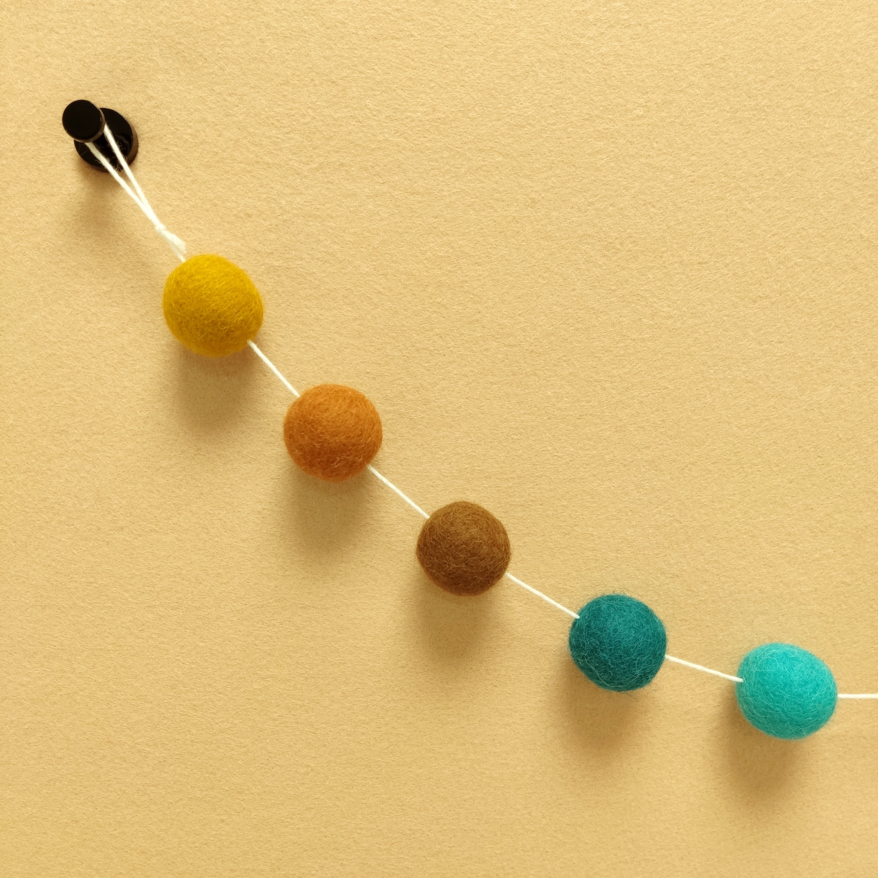 Détail des 5 couleurs de pompons feutrés brun noisette, terracotta cuivré, ocre doré, bleu turquoise et vert canard