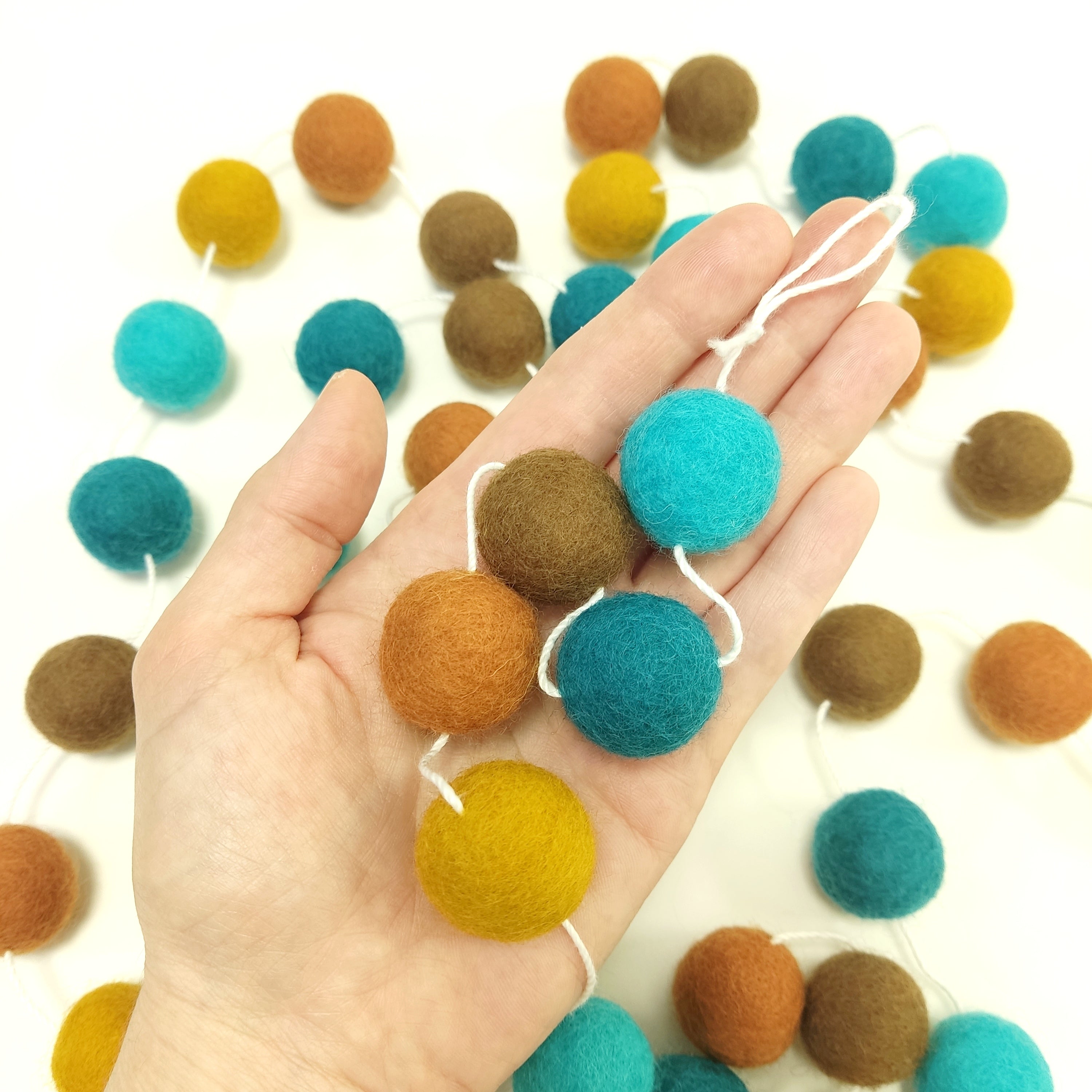 Zoom sur les pompons en laine mérinos Marrakech dans une main, teintes riches et orientales