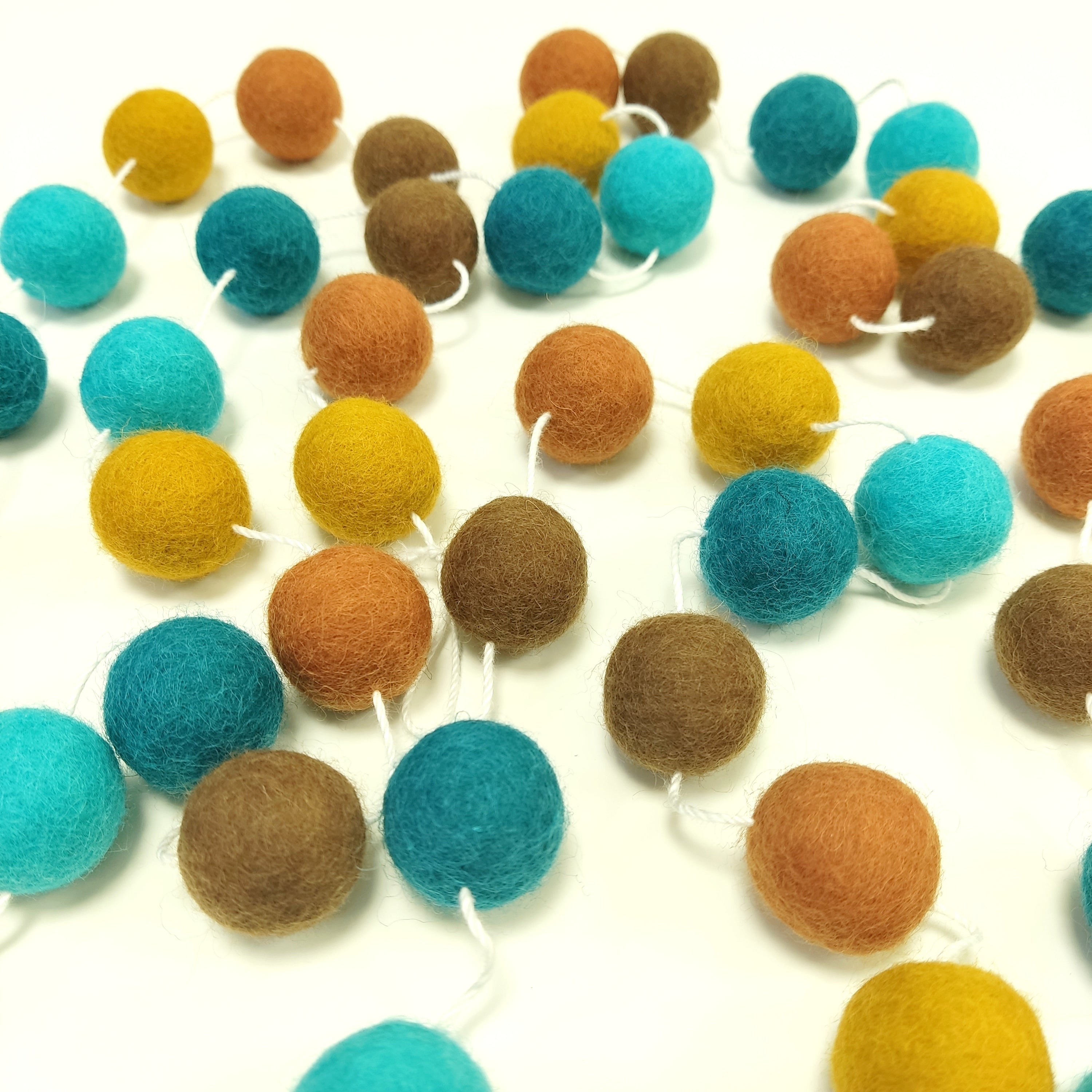 Guirlande de pompons feutrés Marrakech étalée sur une table avec les pompons espacés sur le fil